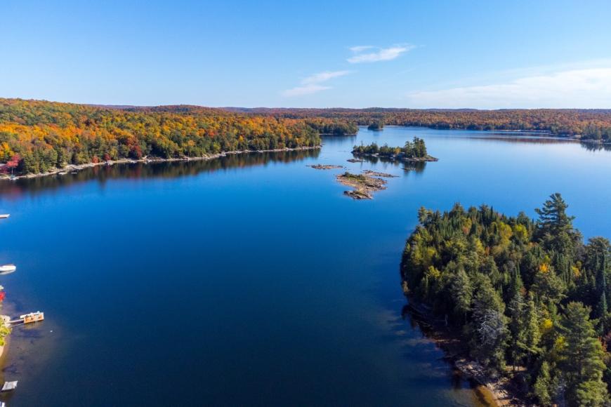 Birds eye view of the dark waters and sandy shores of Kennisis Lake as well as rocky islands and outcroppings.