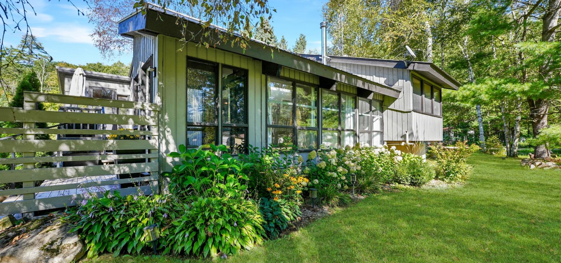 Grey home with bushes out front and green grass. 