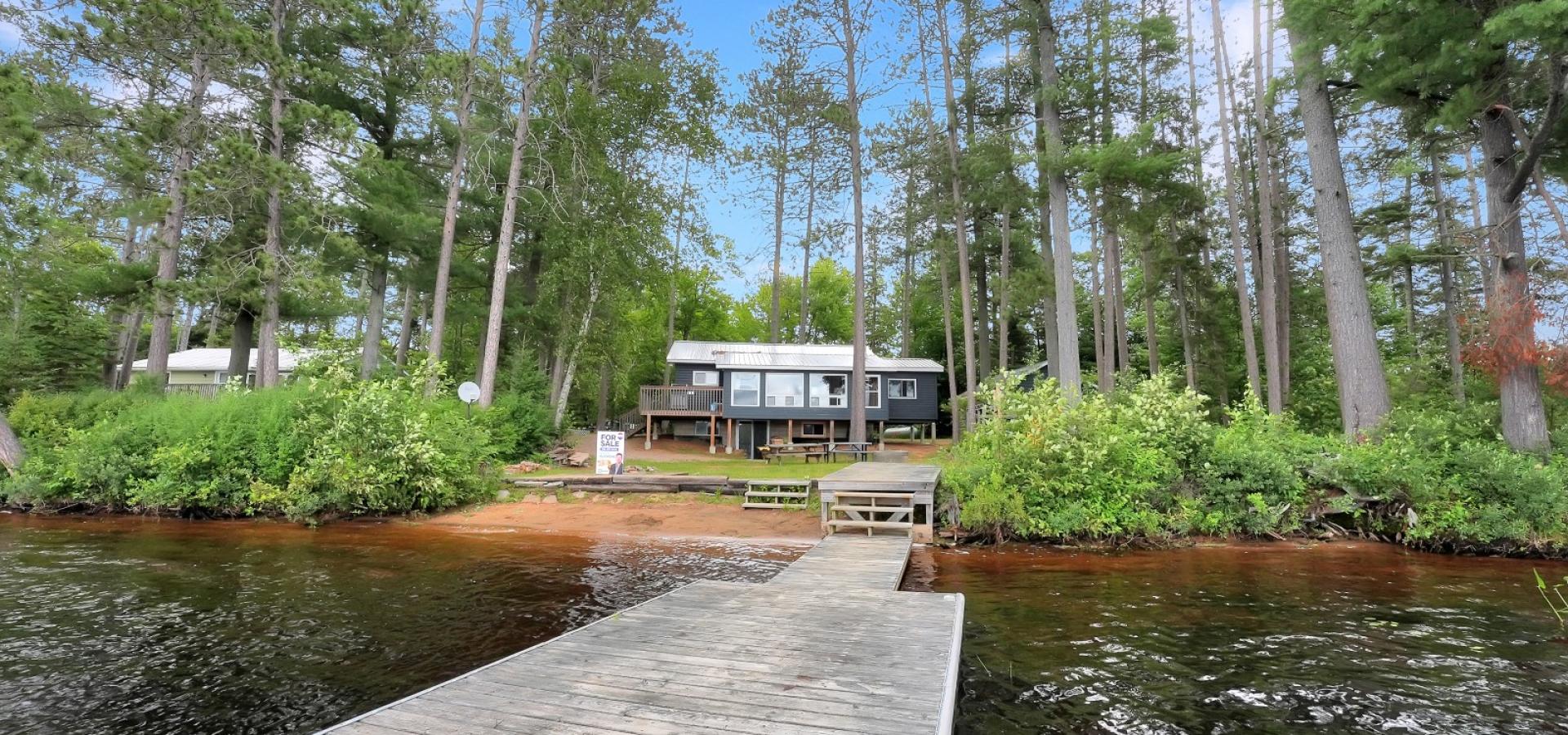 View of a gray cottage from standing on the dock, sandy beach