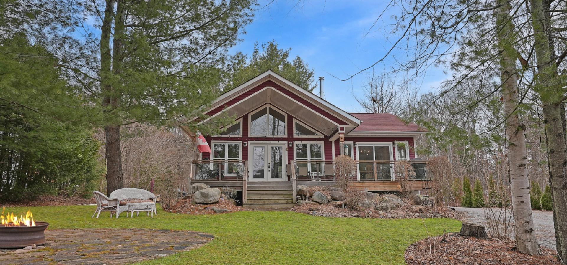 Red home with stairs leading to covered deck, green grass and trees around it.