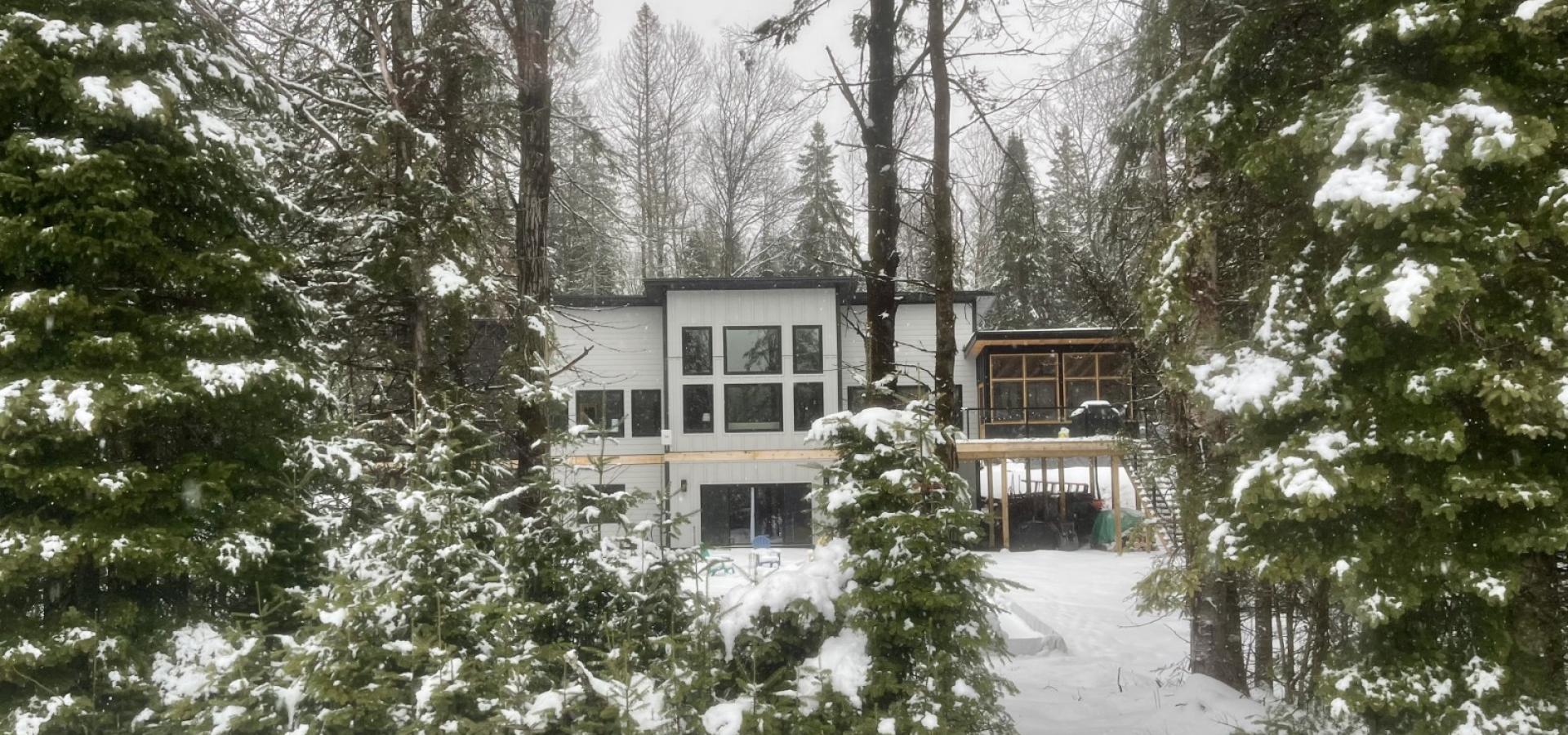 white house with snow covered ground and green trees in front.