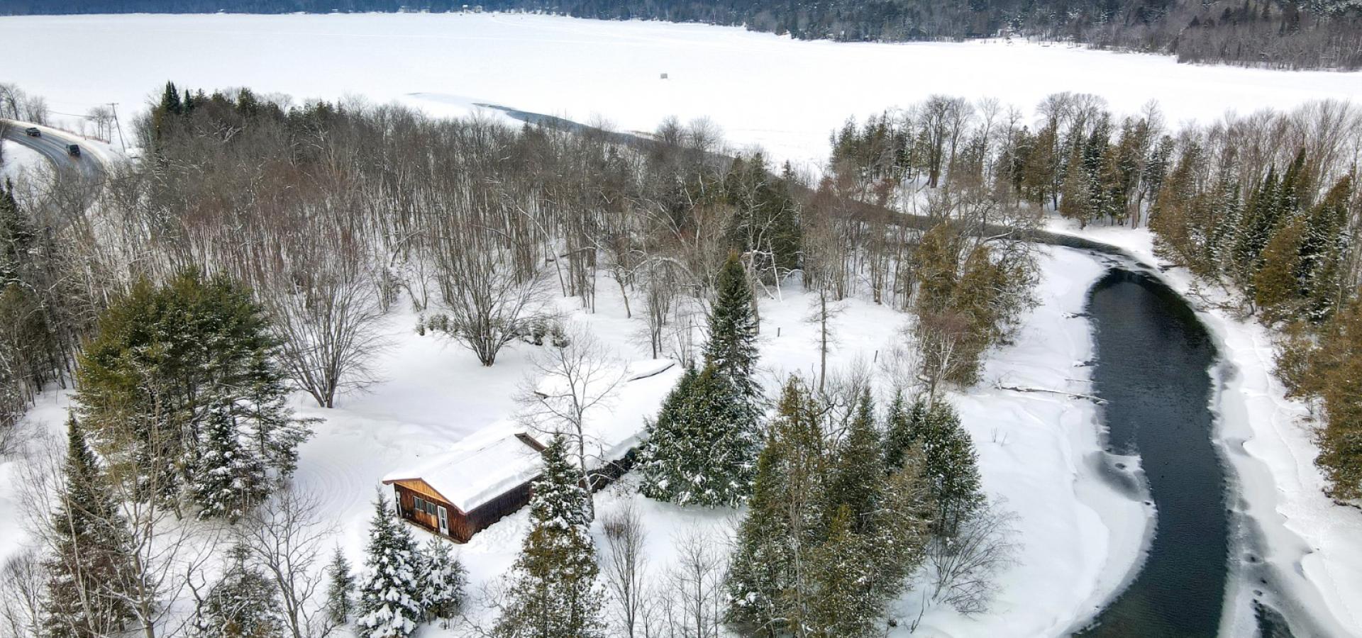 House surrounded by trees with a river leading to the lake. Snow on the ground
