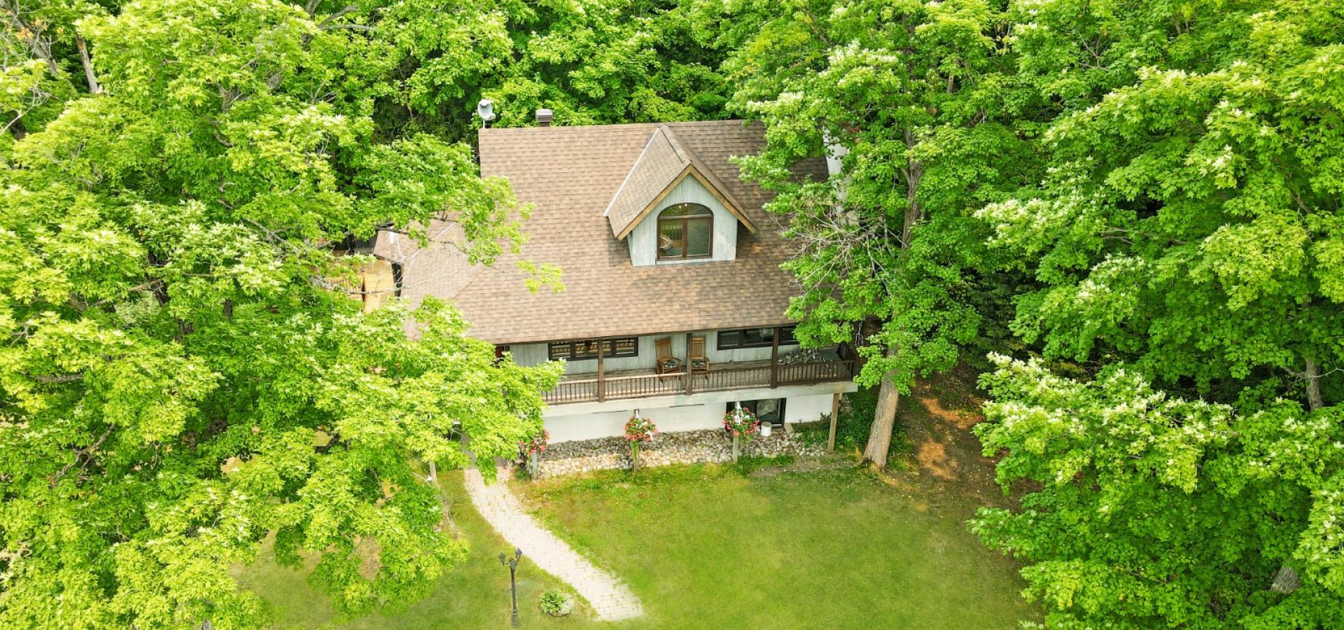 Farmhouse surrounded by trees with a covered front porch and 2 rocking chairs.
