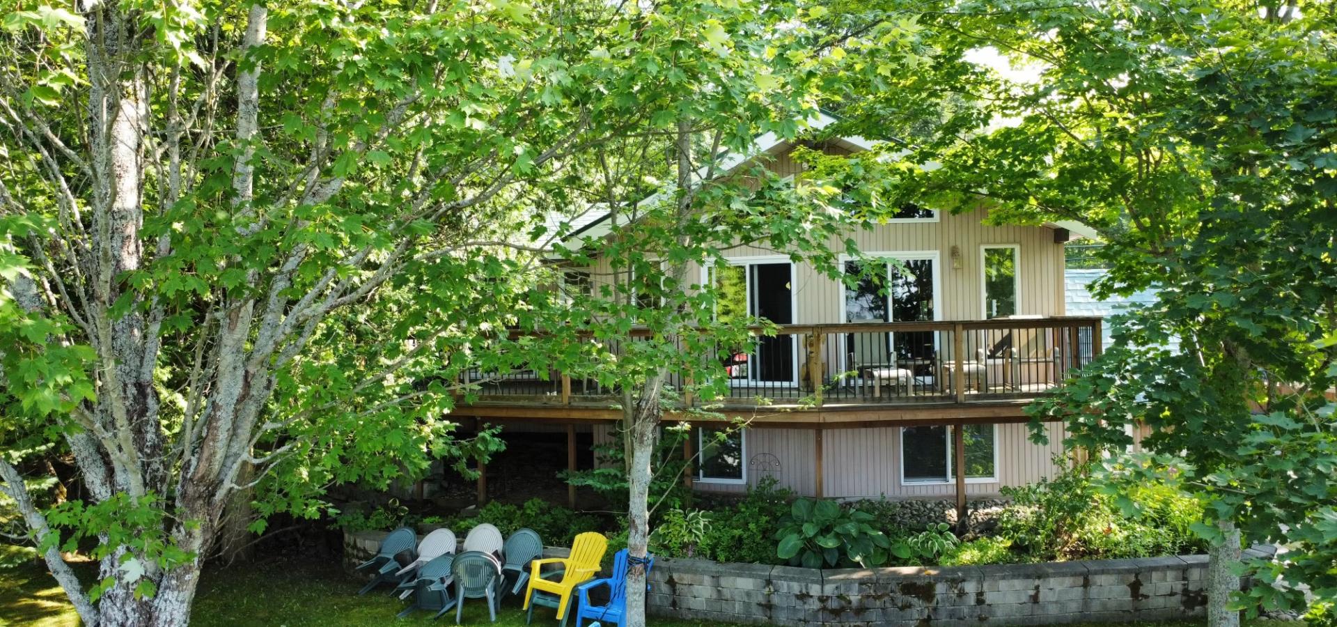 cottage with deck hidden behind trees with green grass