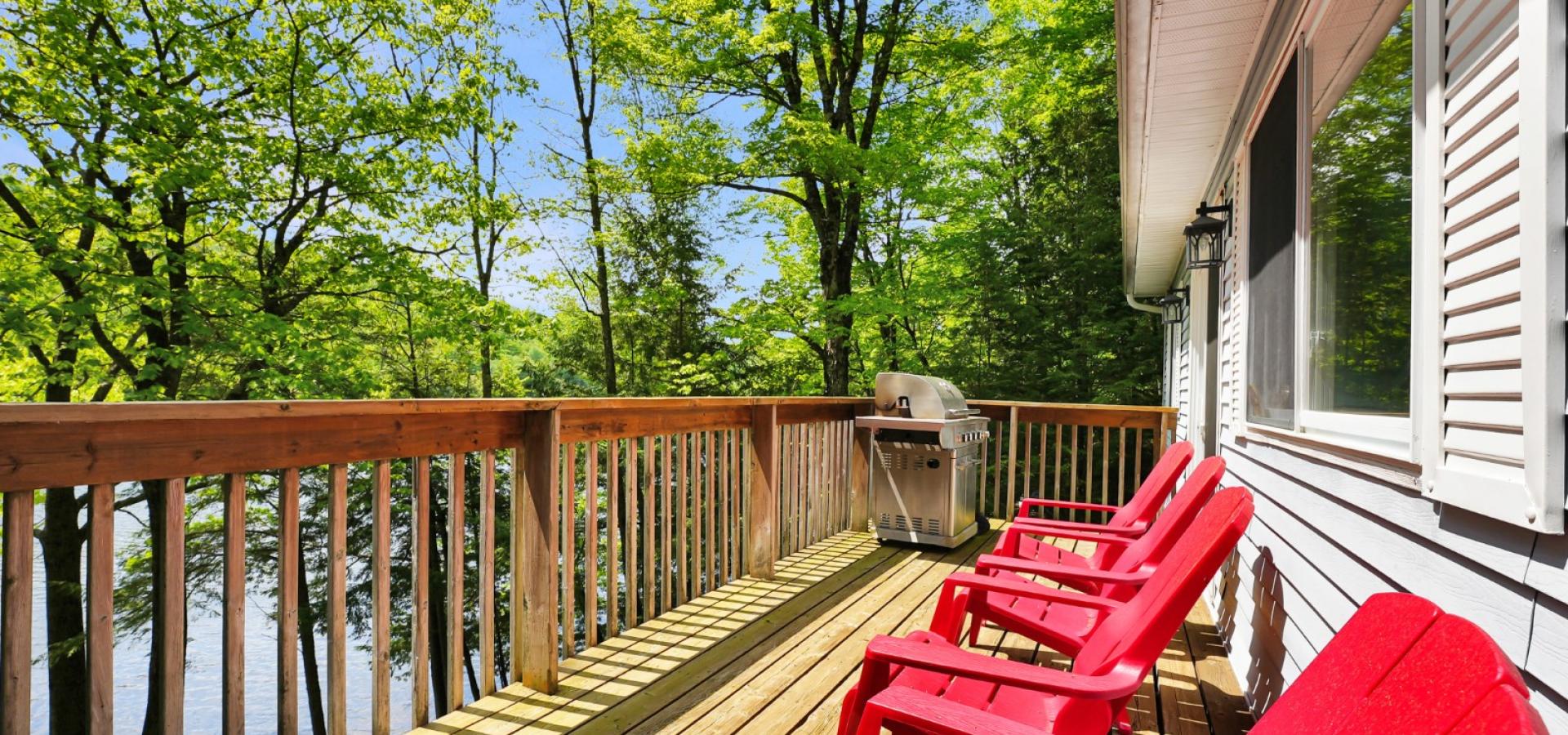 4 red muskoka chairs on a deck overlooking the lake through trees. 