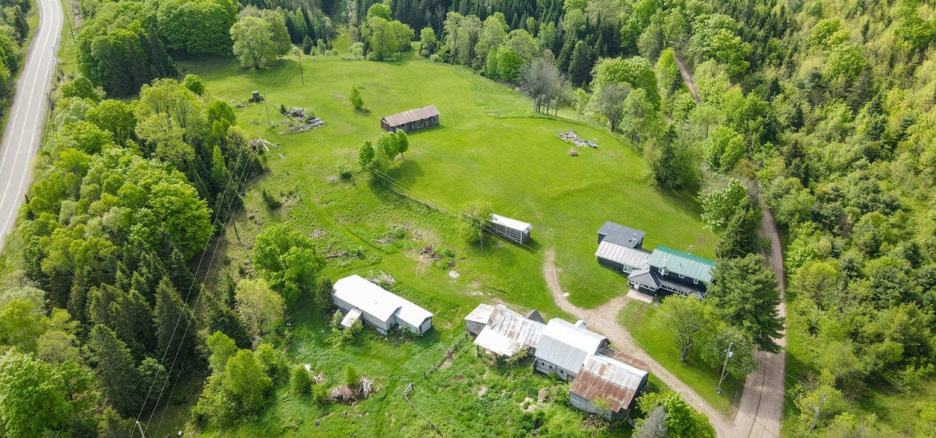 Aerial view of a farm surrounded by trees showings 7 buildings