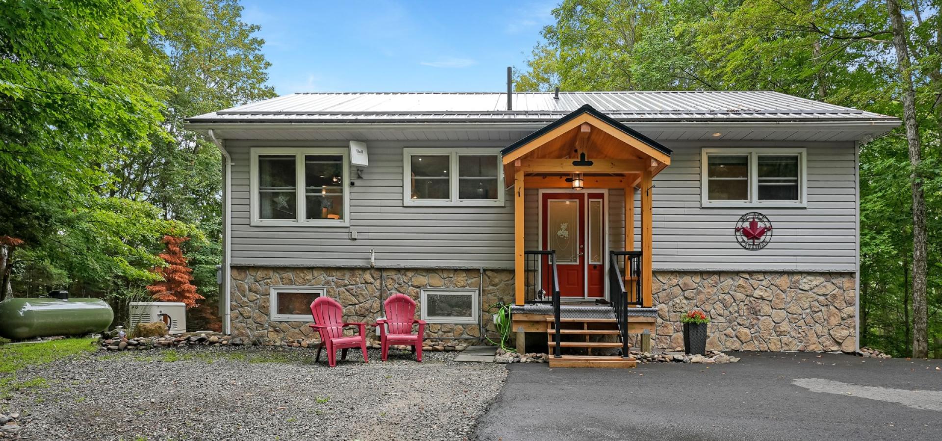 stone and grey home, covered front porch with red door and 2 red muskoka chairs
