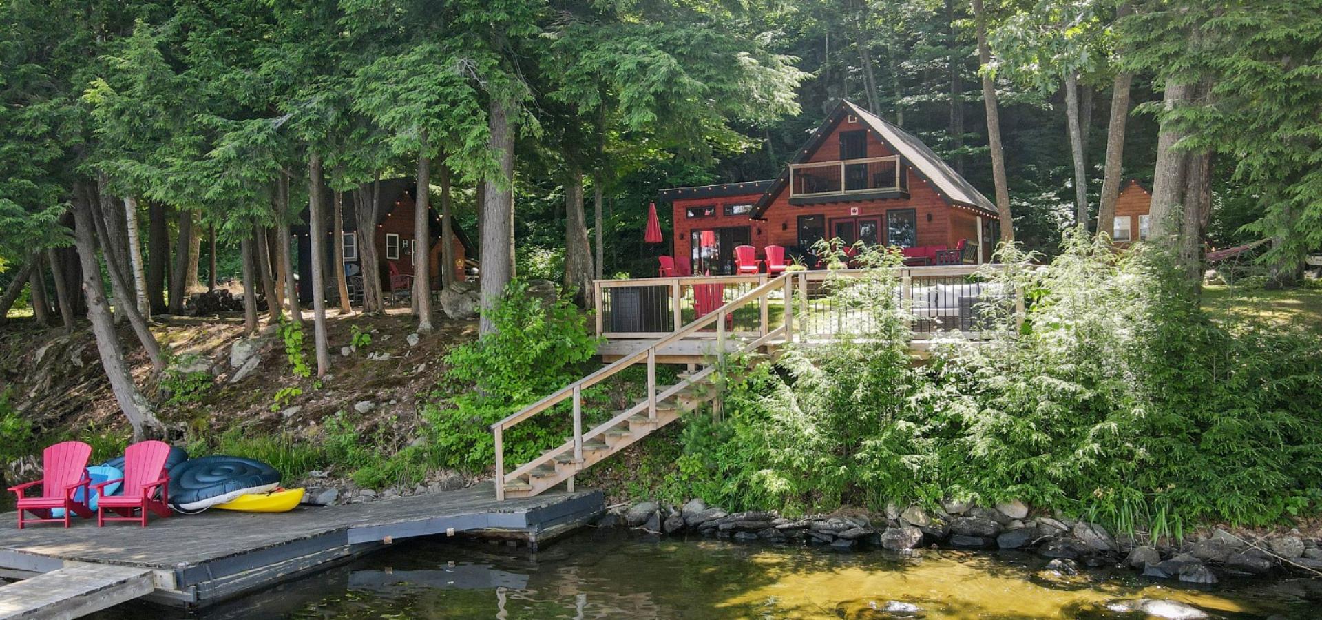 Cottage surrounded by forest, lakeside dec with stairs leading to dock and lakefront.