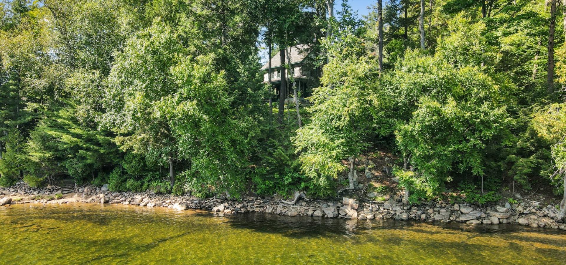 Log home surrounded by mature trees and stone stairs leading to the waters edge