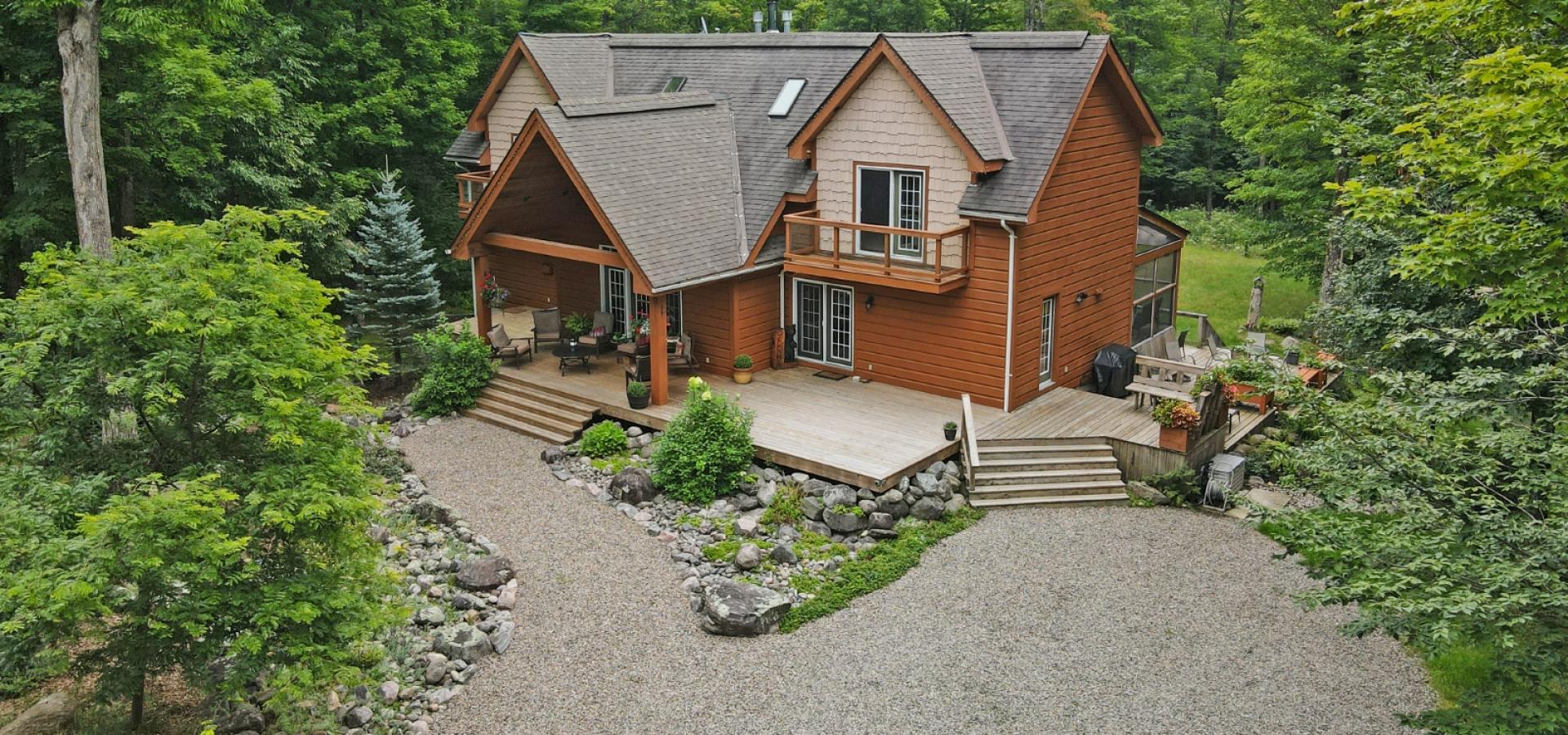 2 story home with a large, partially covered front porch. Gravel laneway and walk way, surrounded by grass and tress.