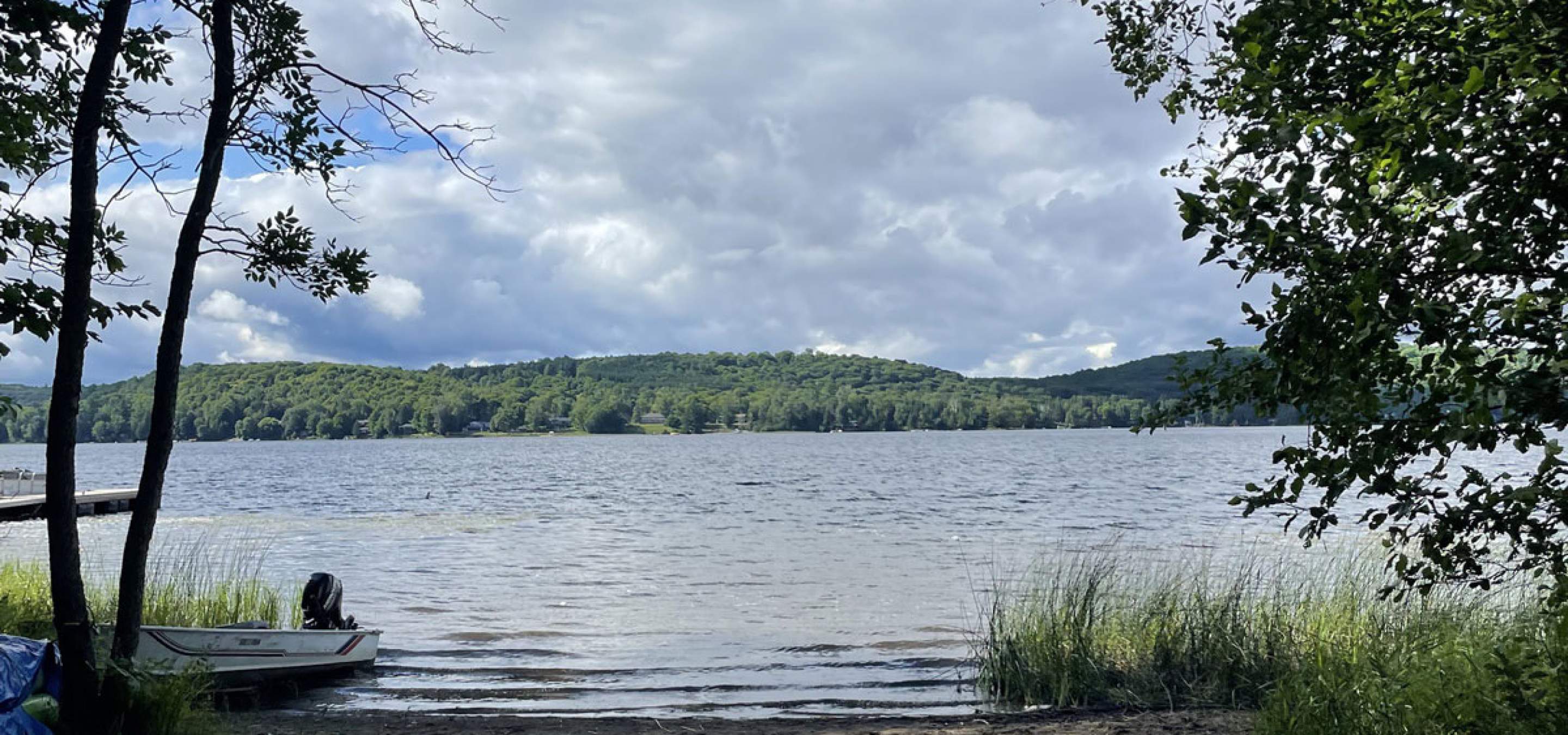 Sand beach and view of a lake with forested hills in the distance and a small motorboat pulled up on the shoreline.