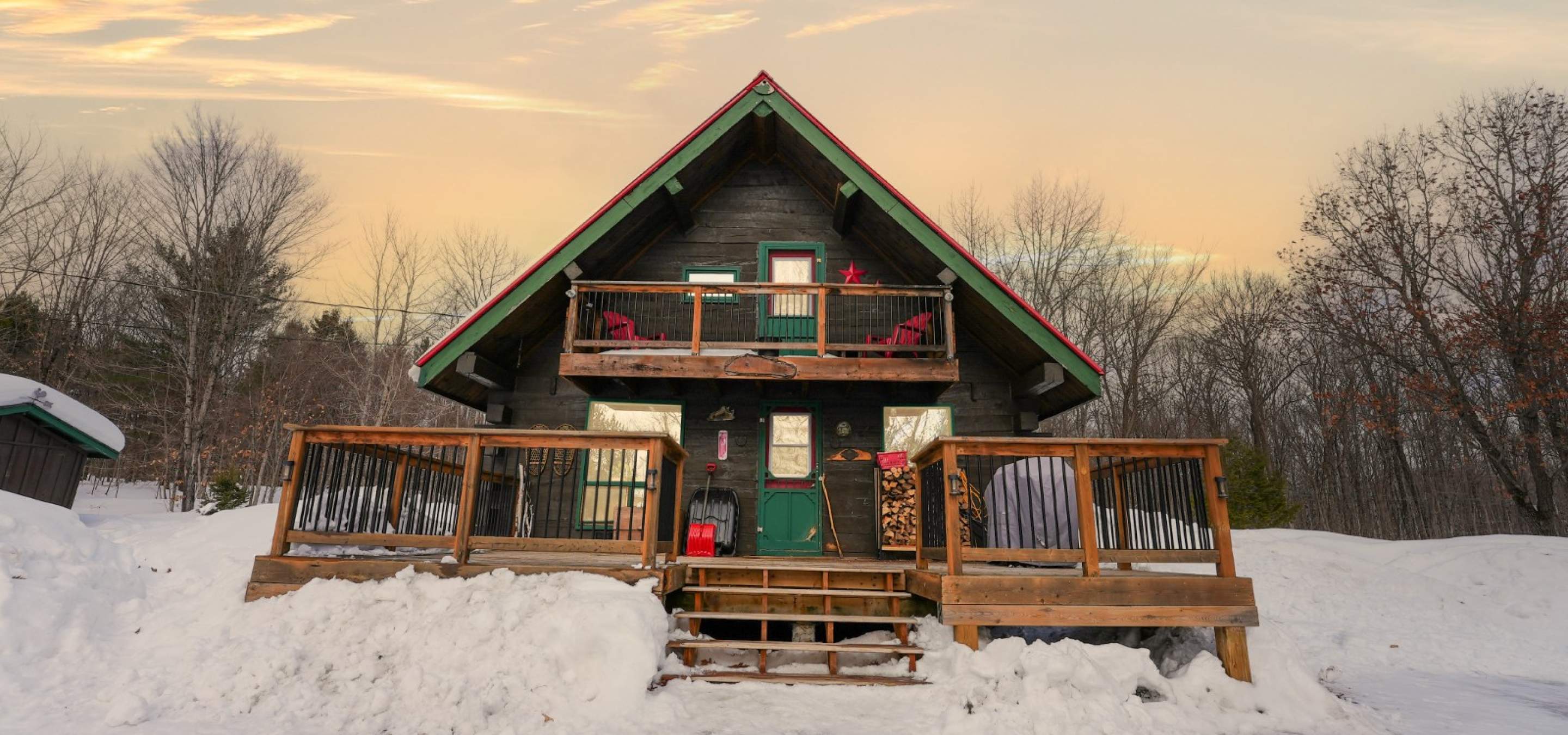 Log home with large front porch and upper balcony, and surrounded by snow.