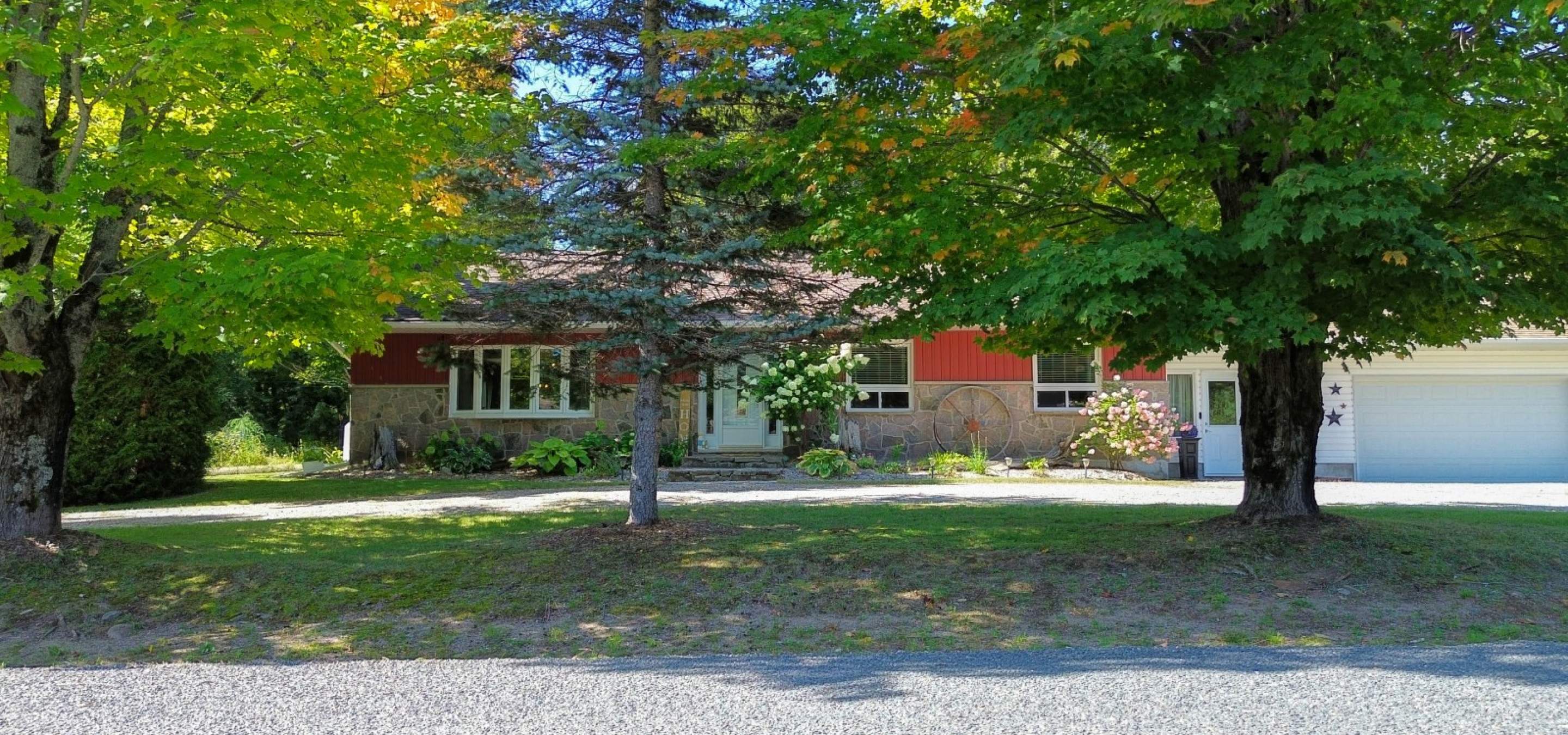 red and stone house hidden behind trees with a white garage