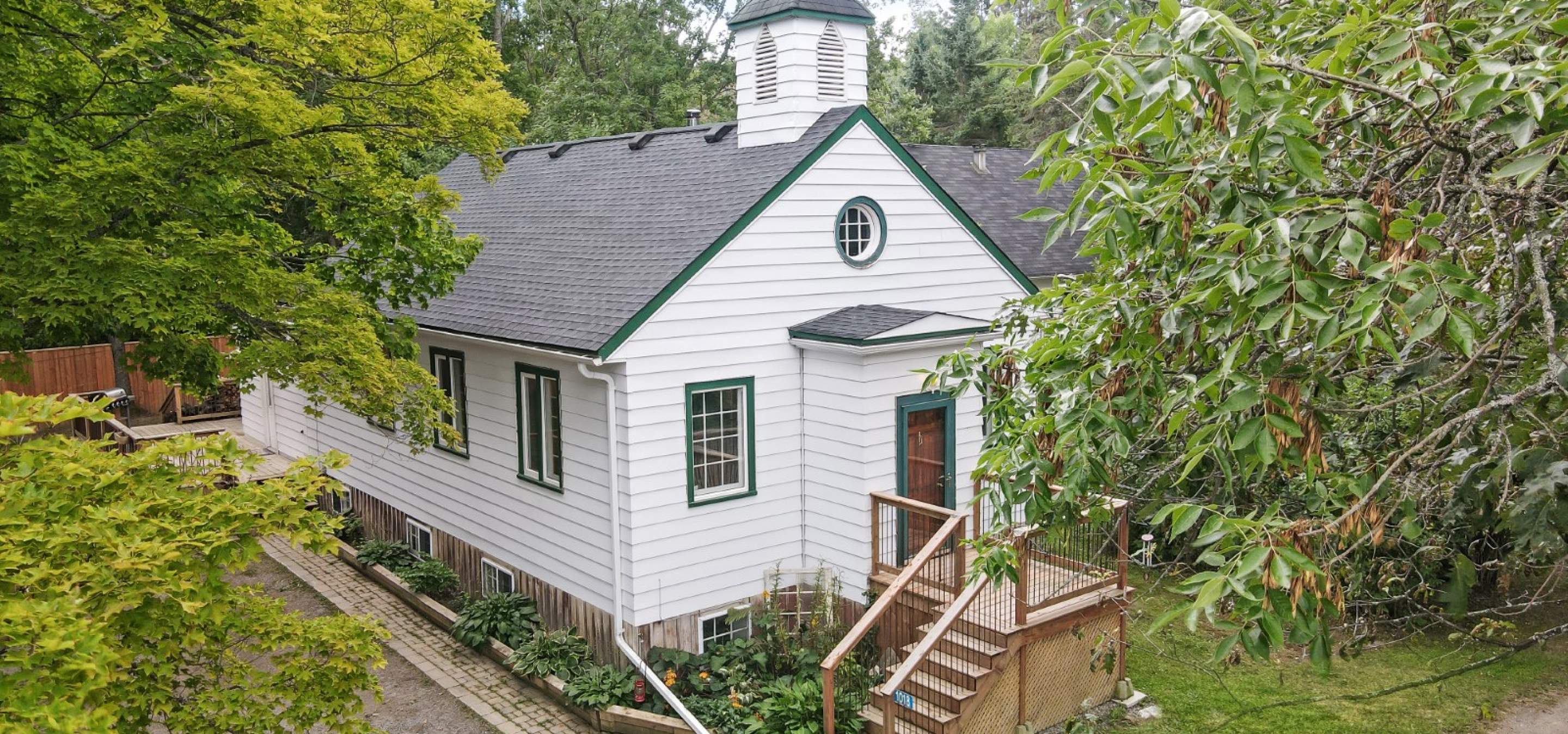 White church style home surrounded by trees and stairs leading to front porch