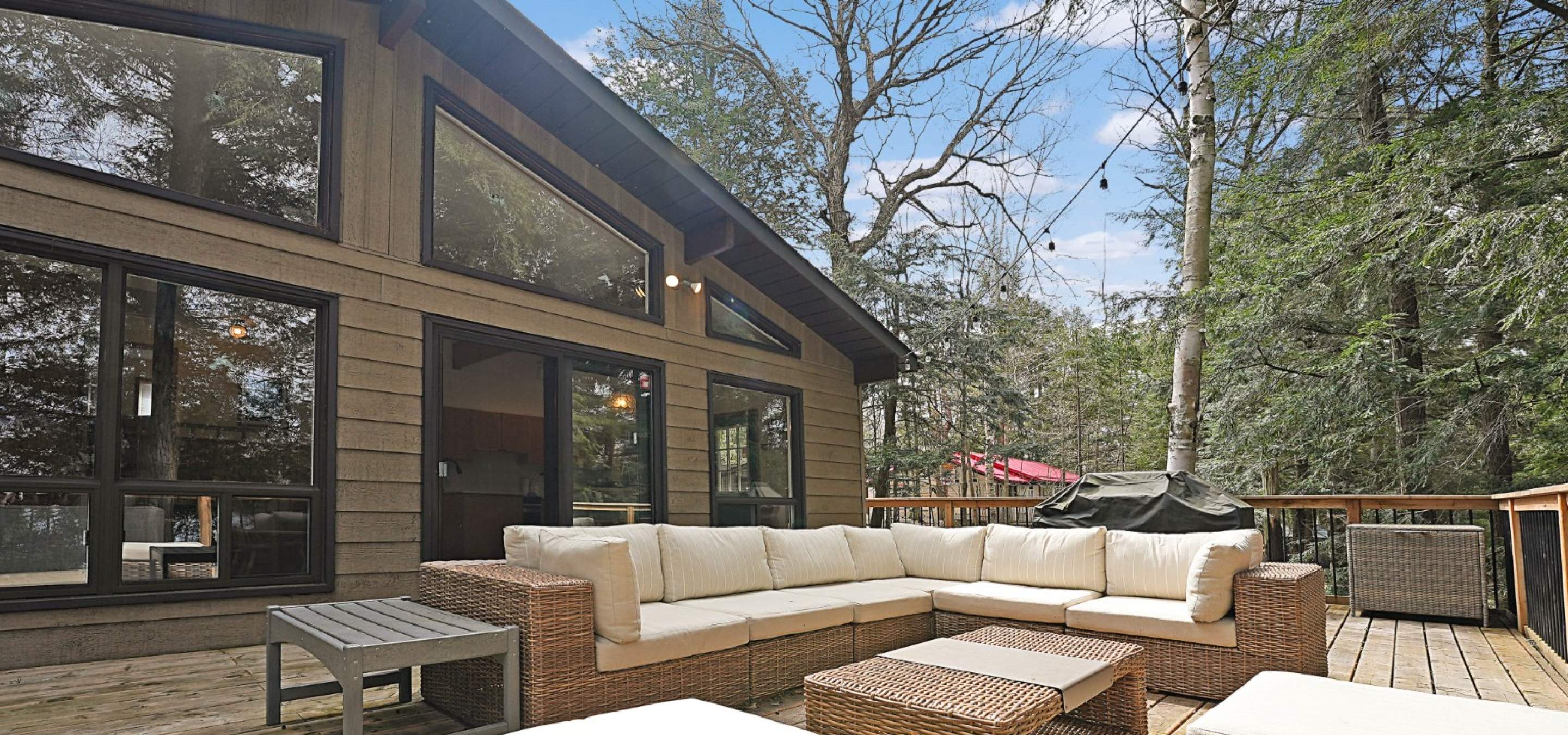 Wood cottage with large glass windows. A deck with lots of seating and a bbq. 