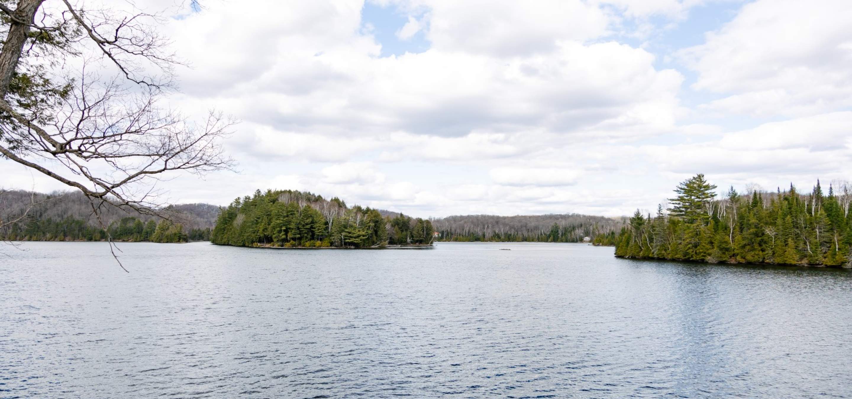 Lake with islands featuring green trees, cloudy sky with some clear blue. 