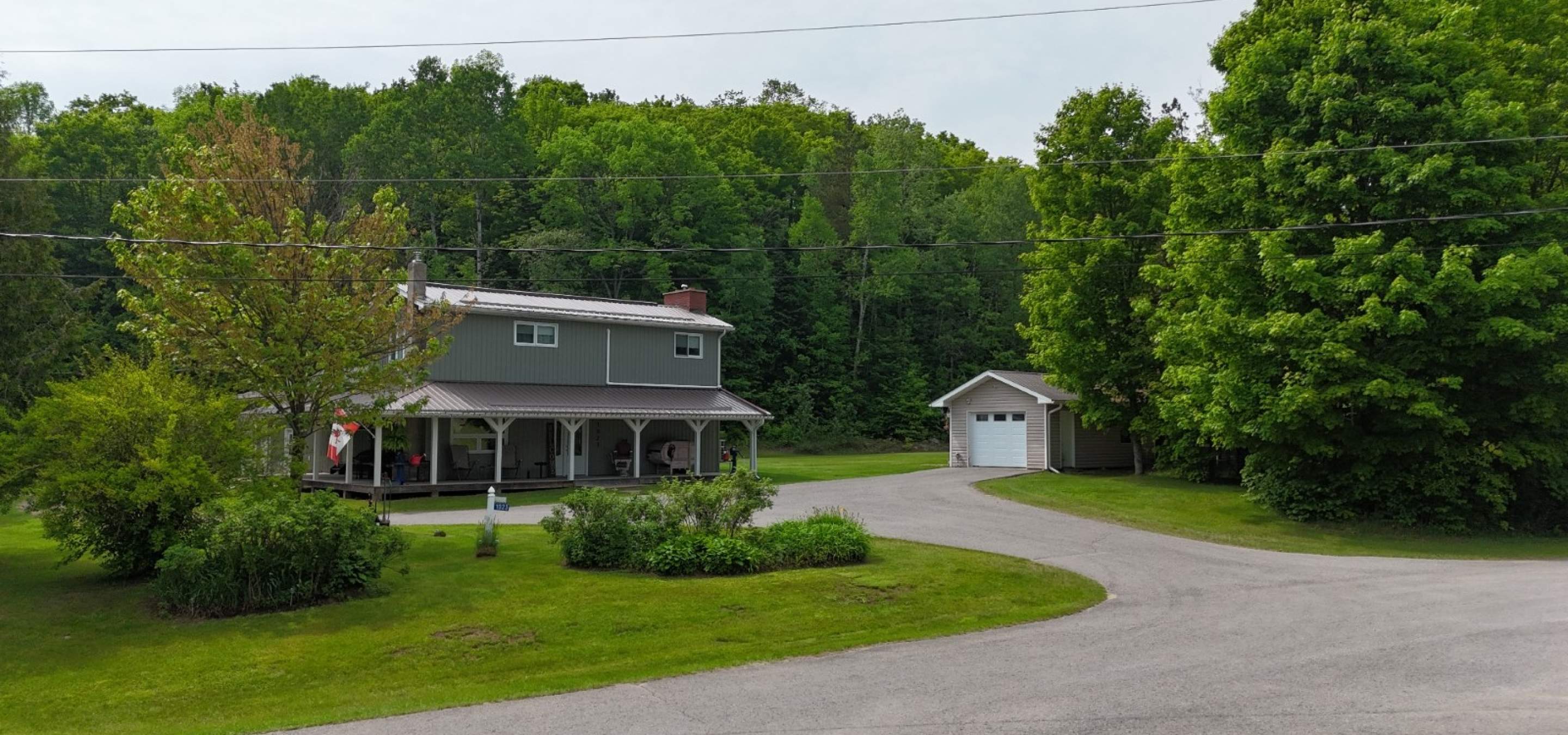 Grey house with full covered porch, detached garage with white door and paved laneway