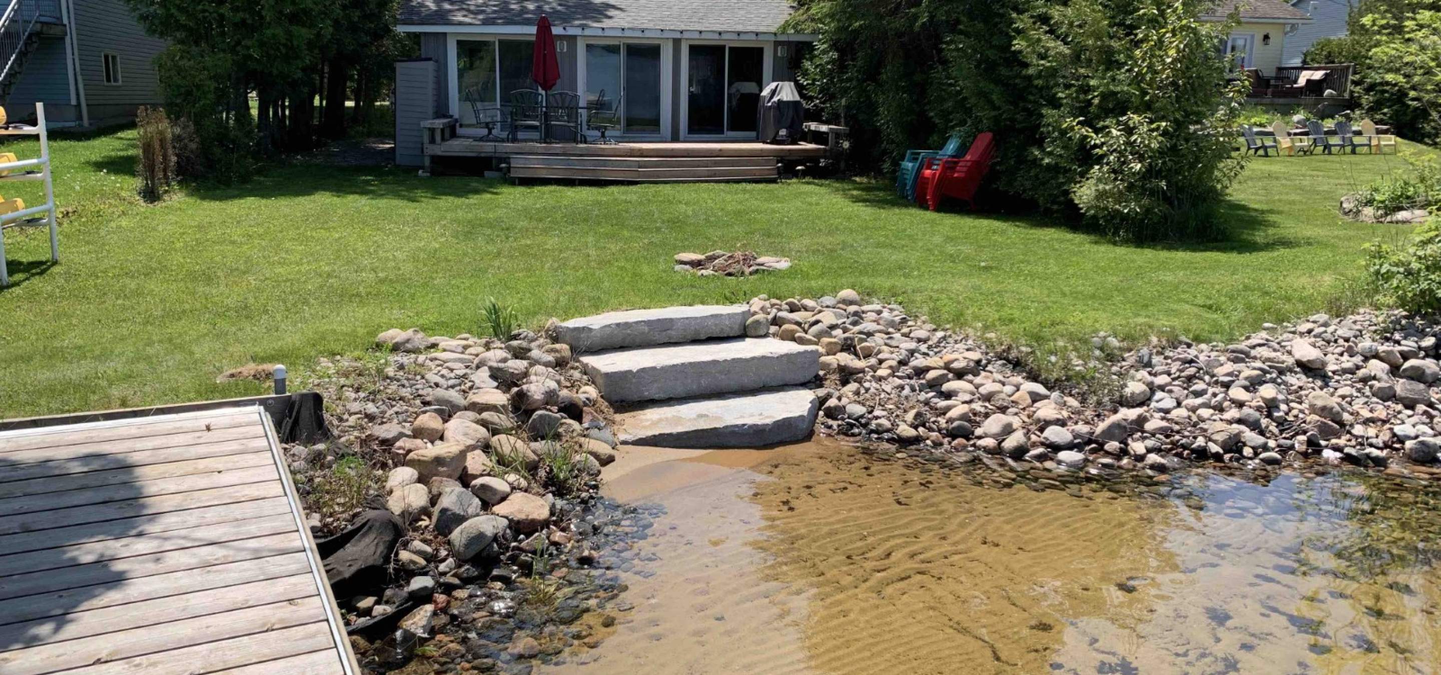Cottage with green grass, shore line with 2 steps down and sandy bottom