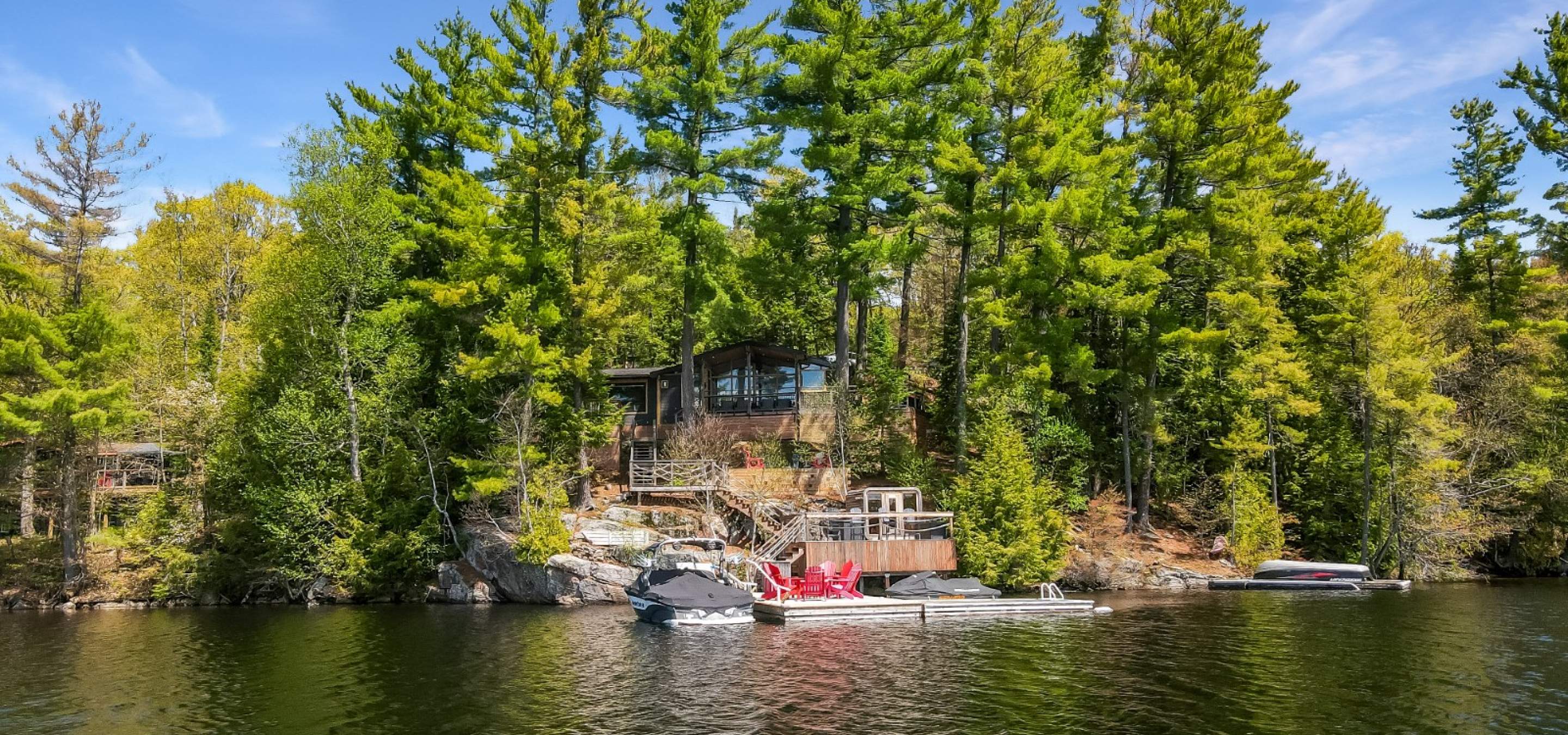 cottage hidden with trees, multi tier decking, red chairs on the dock and blue skies