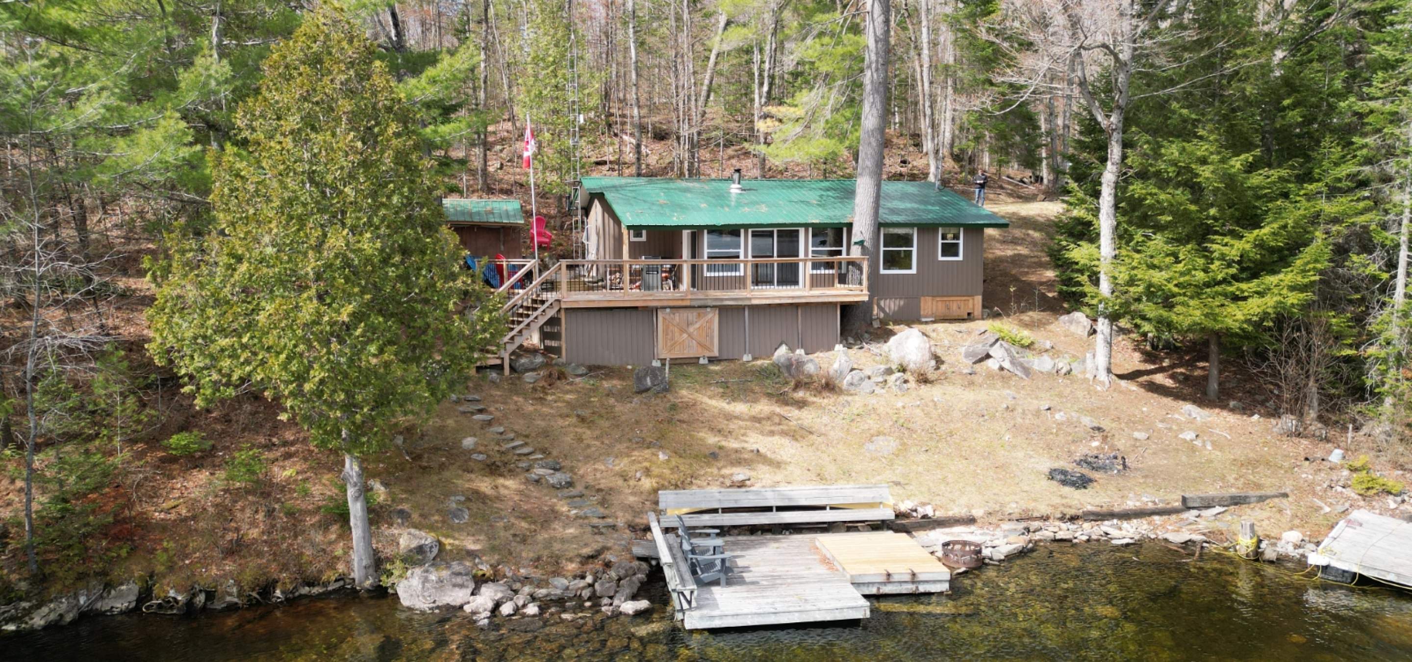 Cottage with a green roof, trees down the side, and dock in the lake