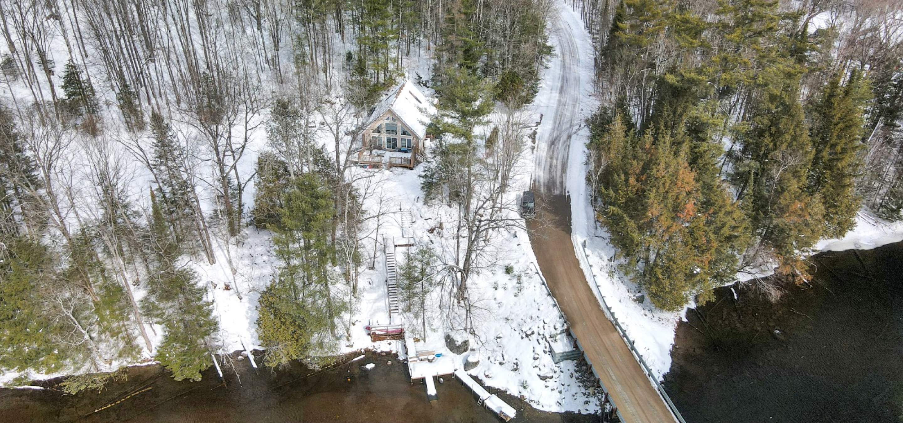 Aerial view of a property with trees, a road, snow and a river