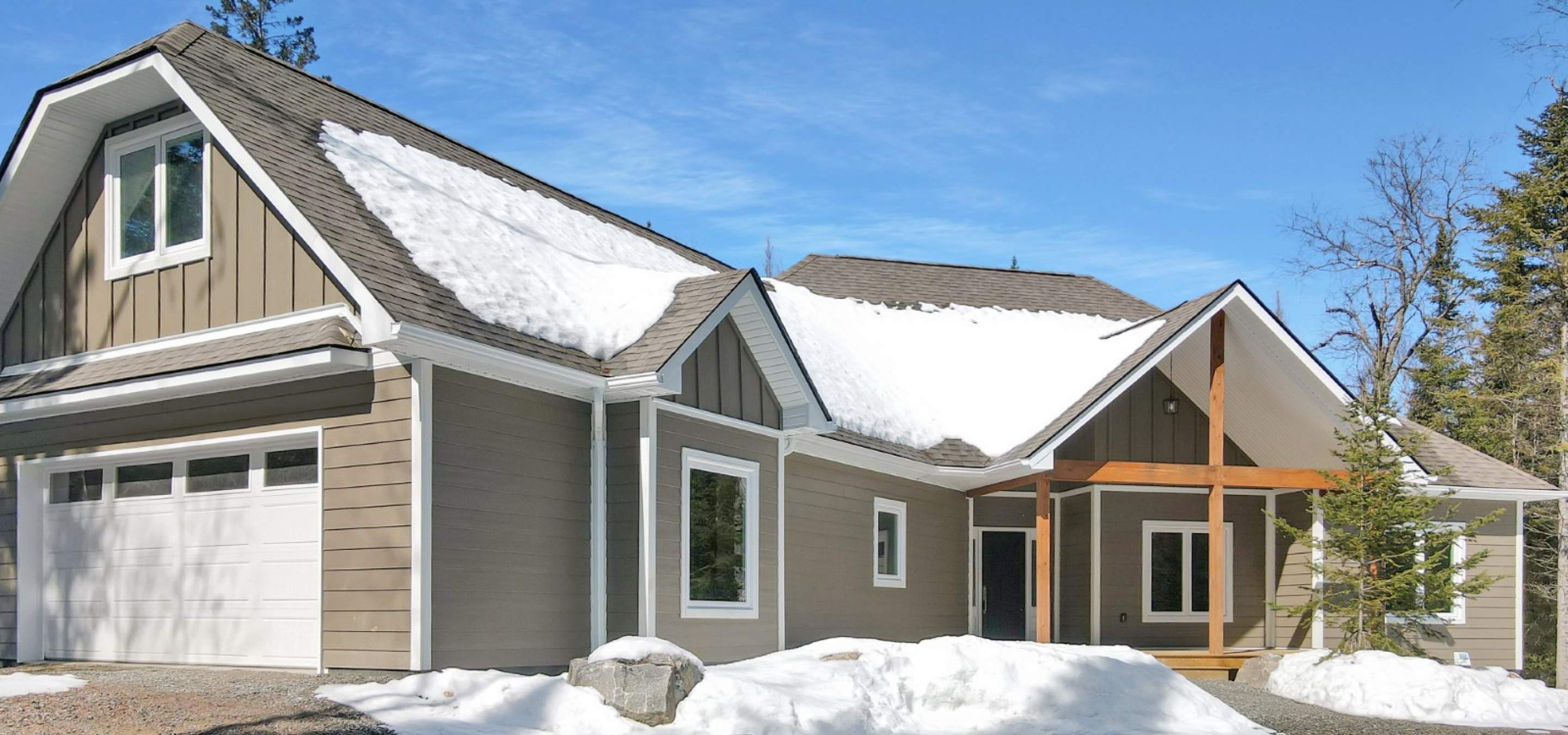 brown and white home with wood framing on porch and surrounded by snow.