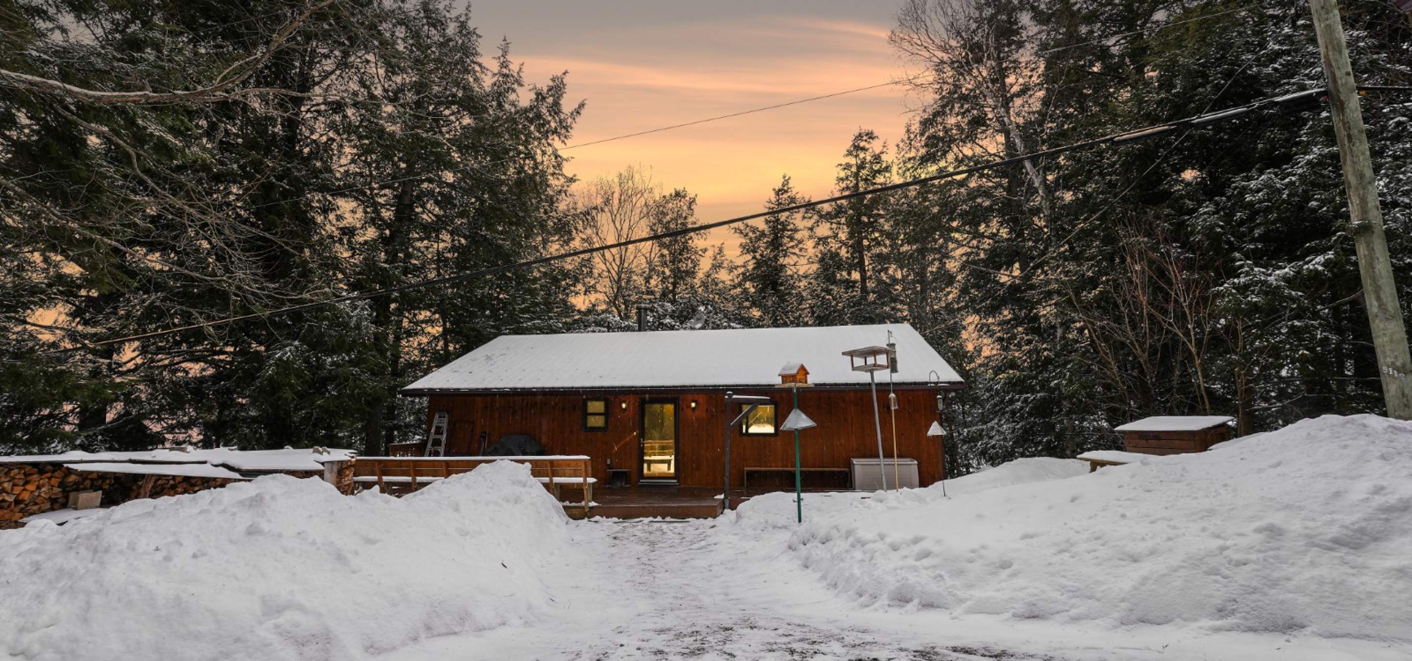 wood cottage with trees on either side, snow in front and sunrise over top