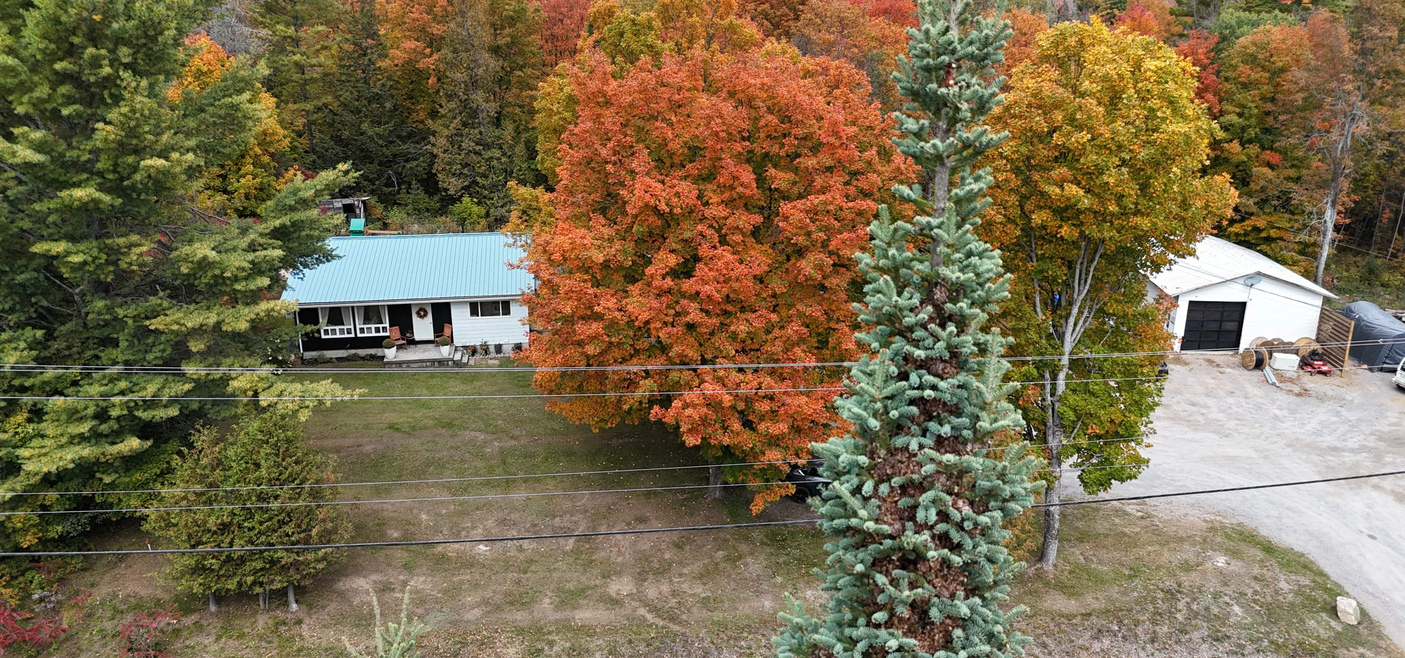 Home with white siding and brown wood siding, white garage on the right, and fall coloured trees.