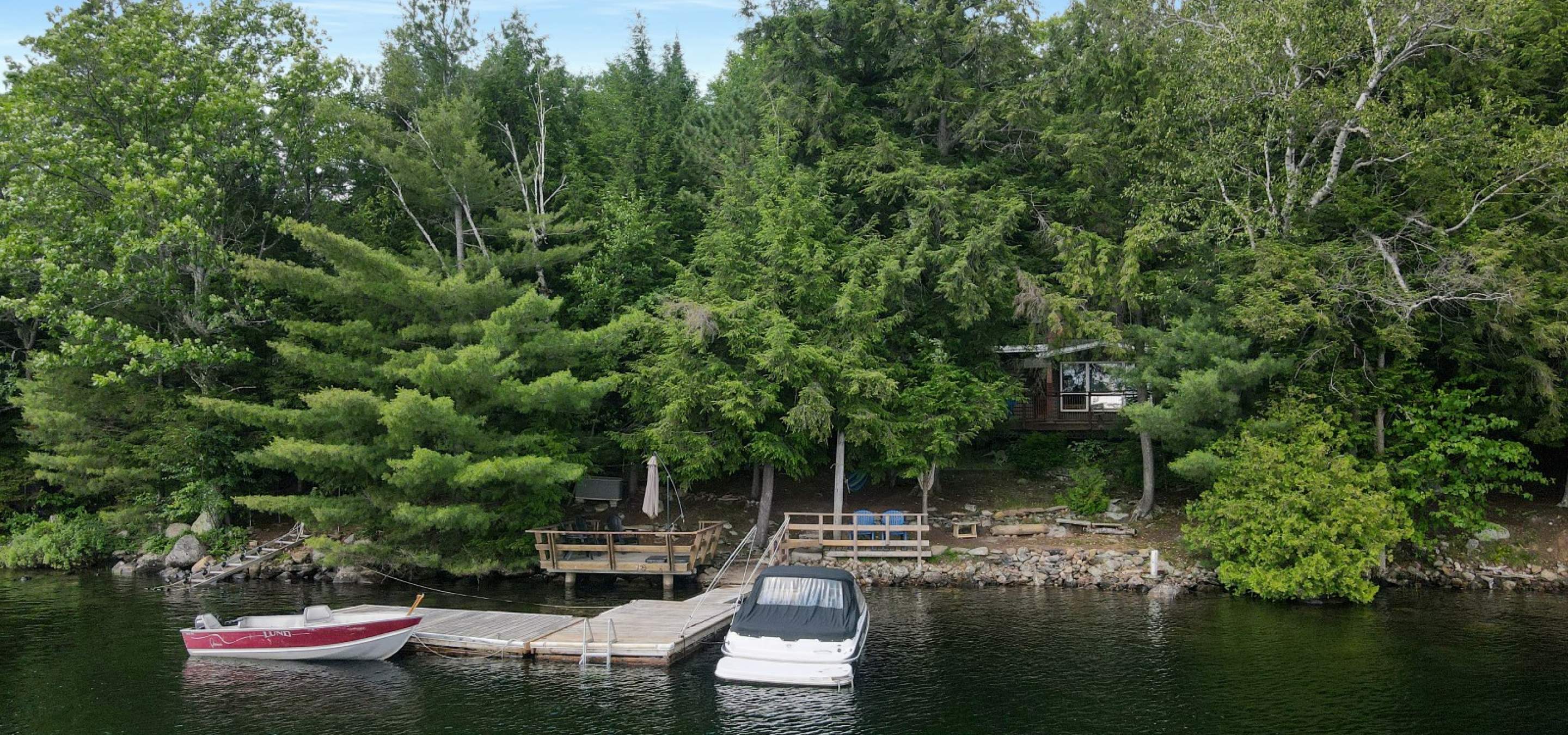 View of a cottage, dock and 2 boats from the lake. 