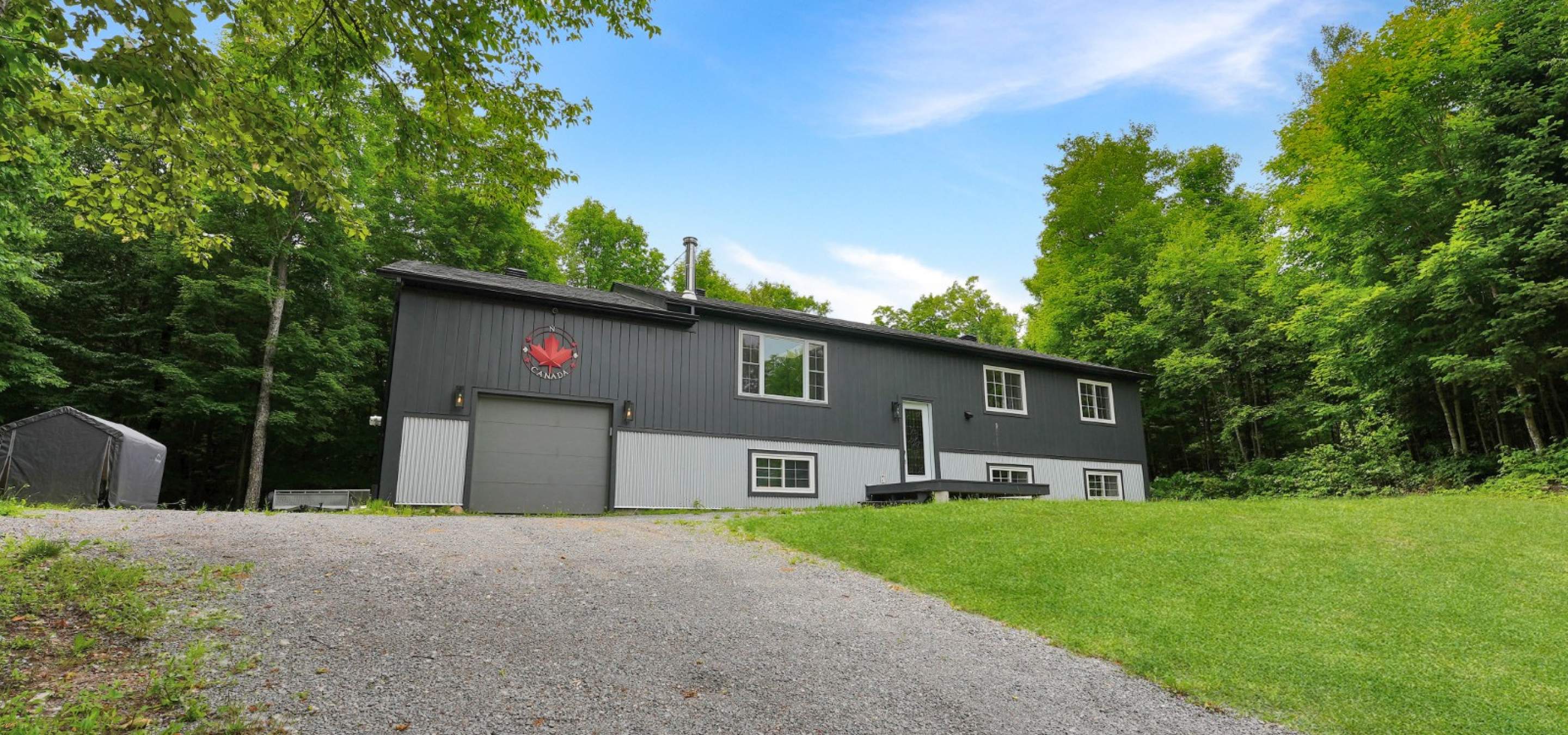 Grey home, single garage door, green grass and gravel laneway