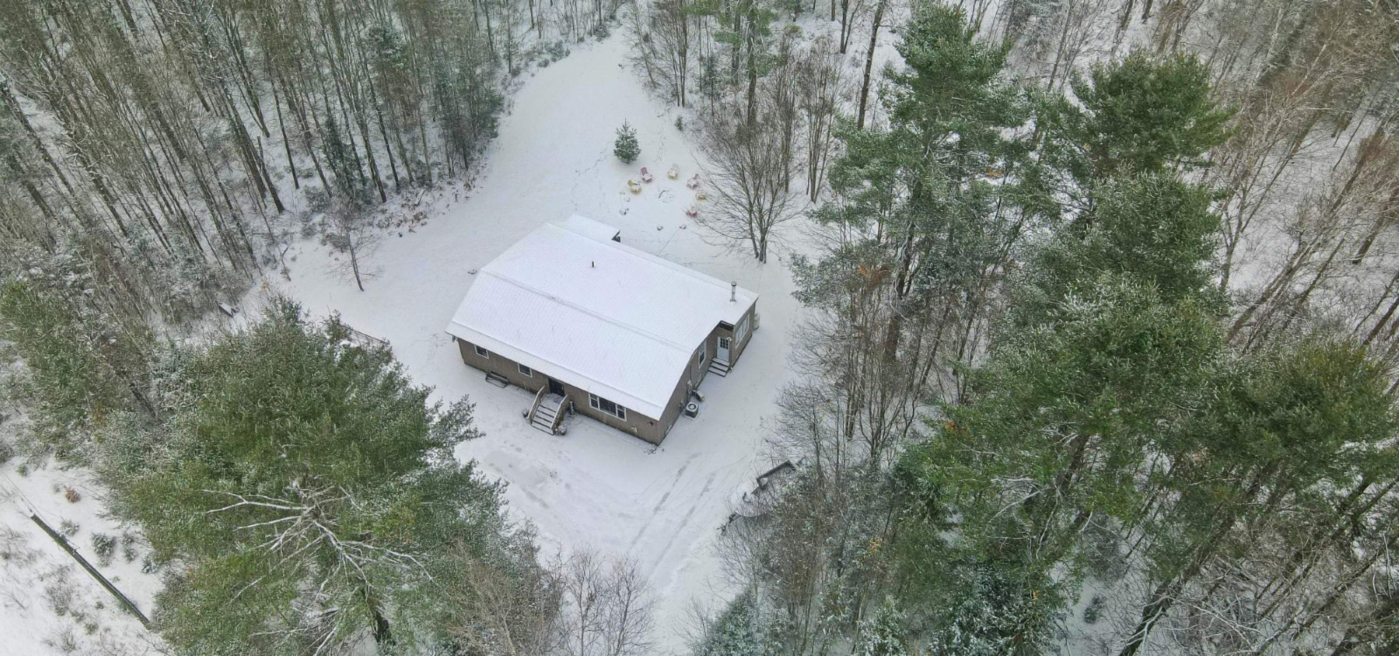 Aerial view of a home with snow and surrounded by trees.