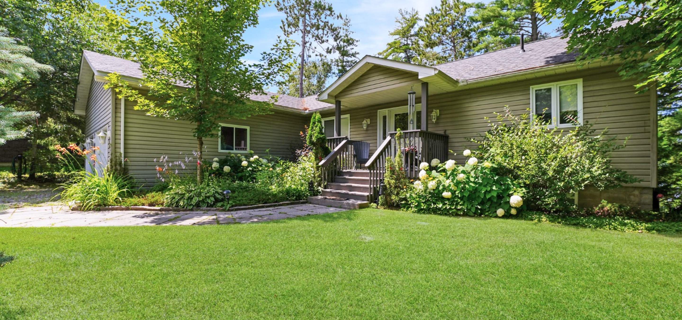 home with covered front porch, full gardens, trees and green lawn out front