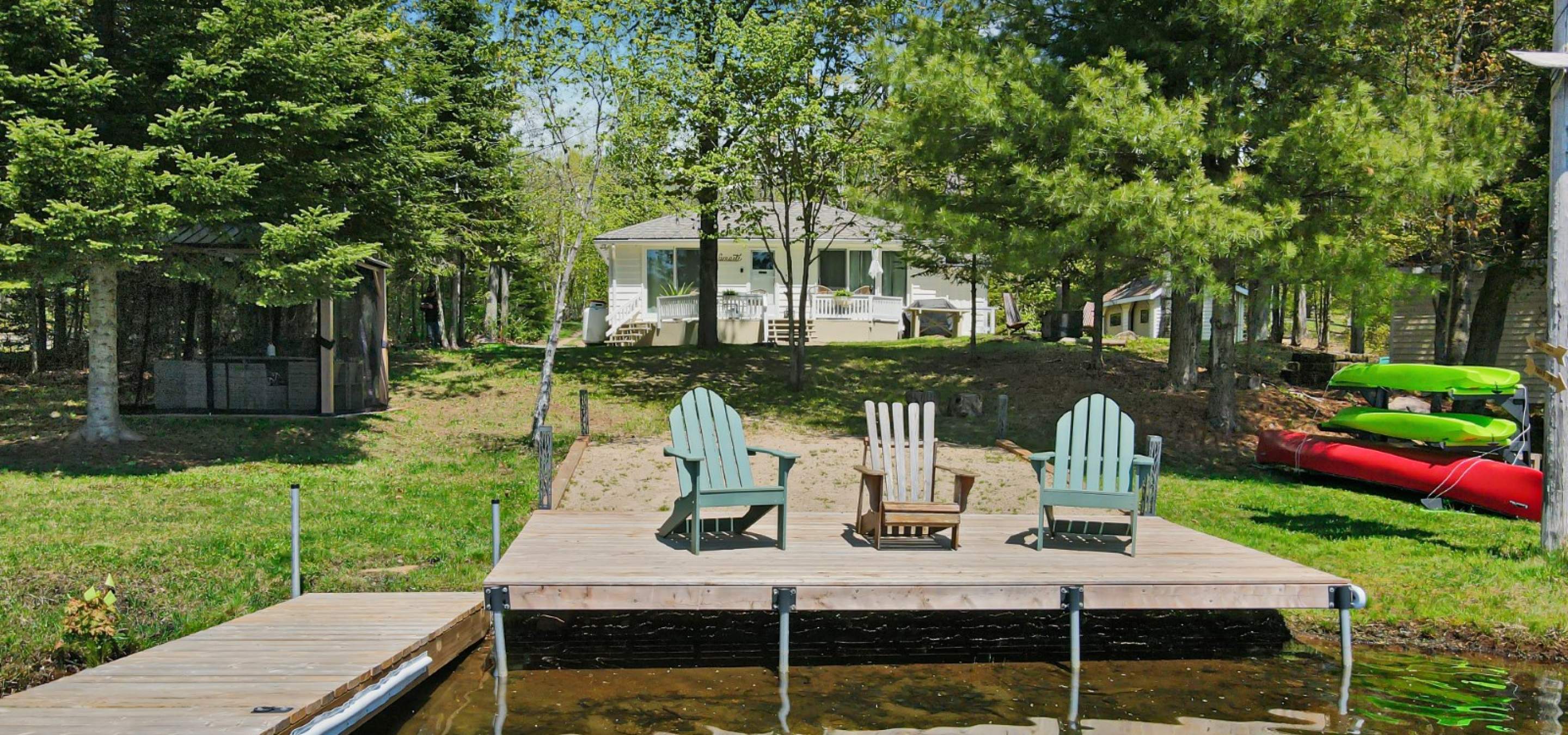 Lovely cottage with 3 Muskoka Chairs on a lakeside dock at the waters edge