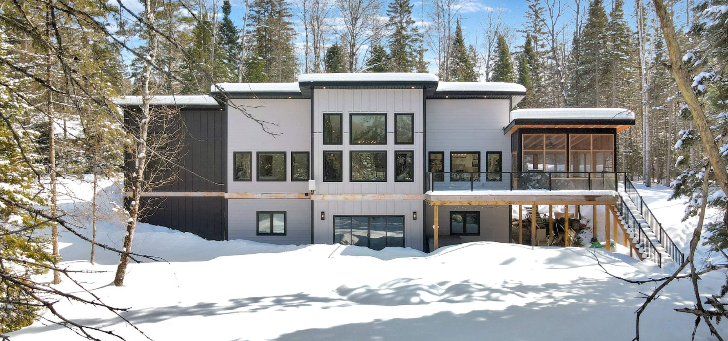 Snow covered ground, grey and black house with screened porch