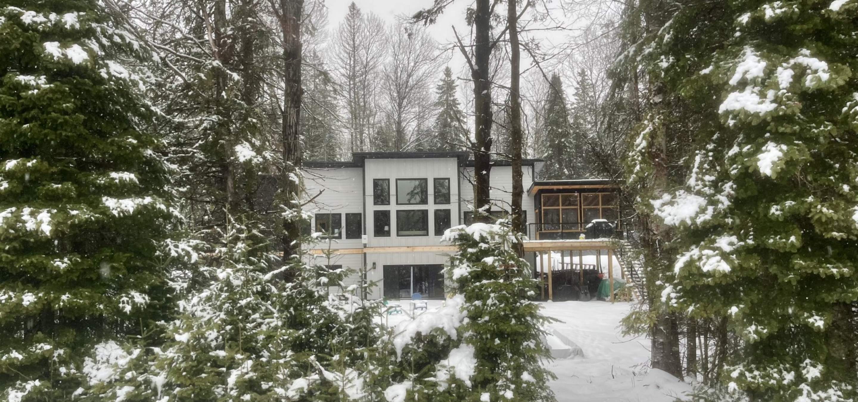 white house with snow covered ground and green trees in front.