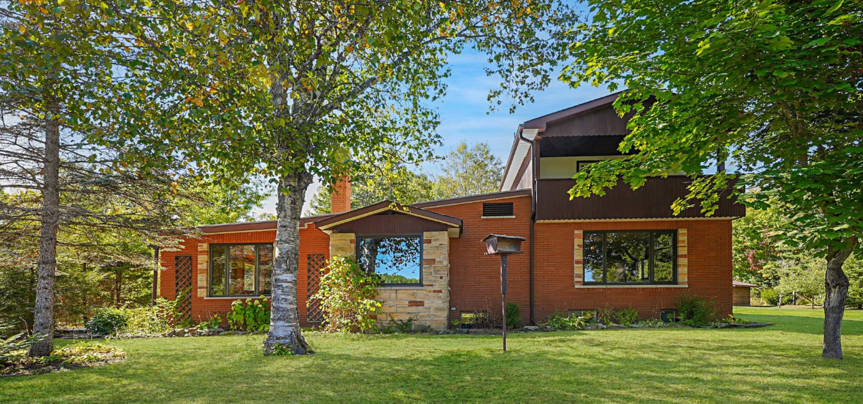 Red brick house shaded by tree and green grass.