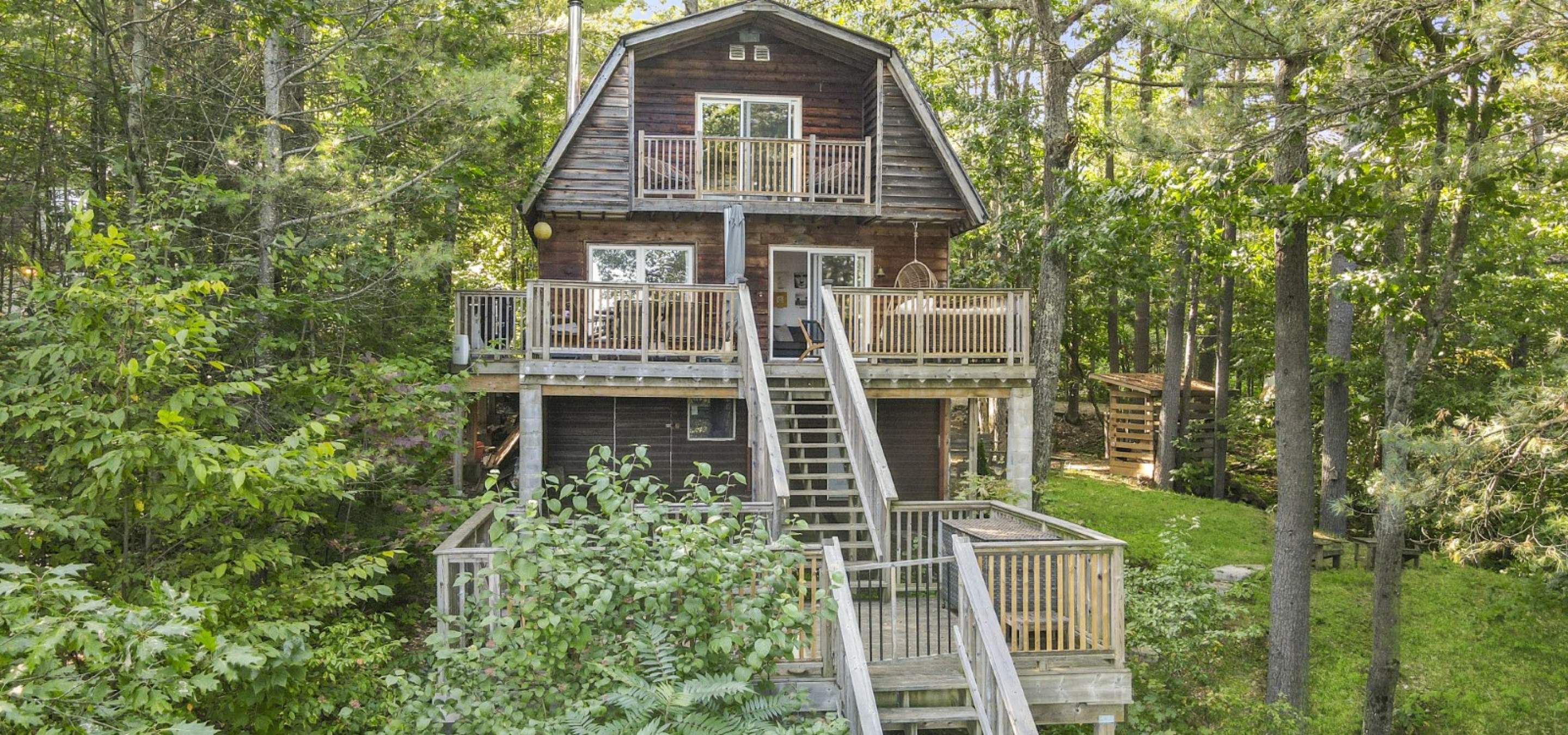 cottage in the tree tops with 3 levels of decking, barn shaped roof and green grass. 