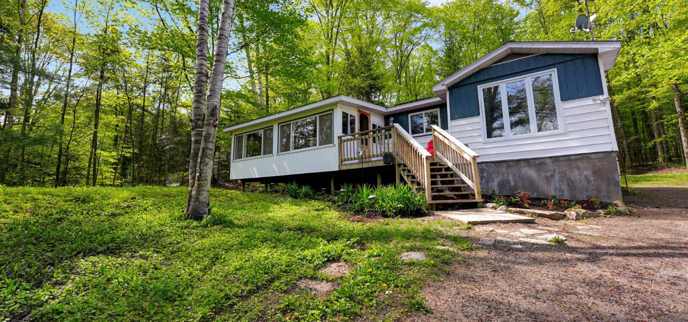 White and grey home with wood front porch, surrounded by trees and green grass.
