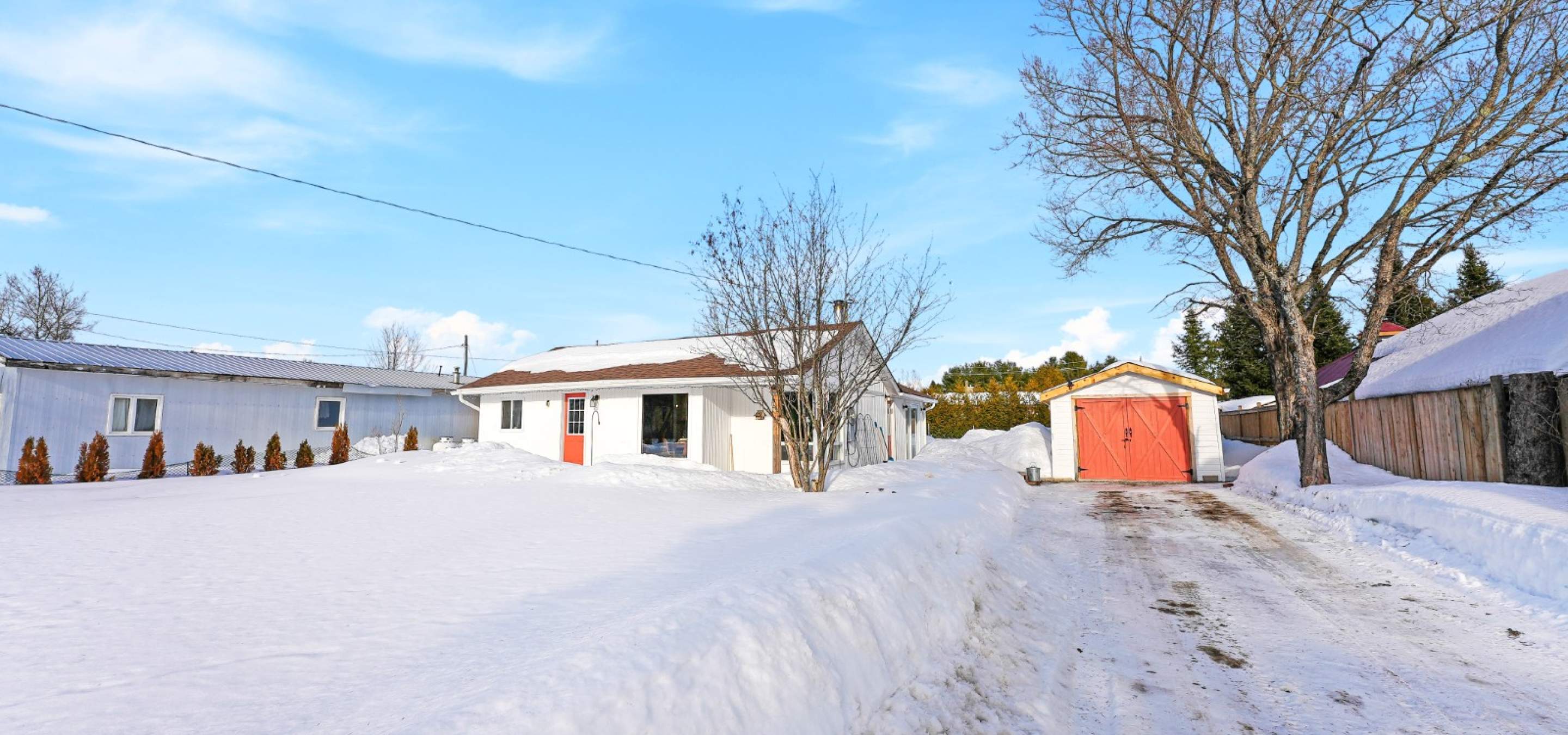 white bungalow with a red door, garage with red door, snow on the ground, blue skies
