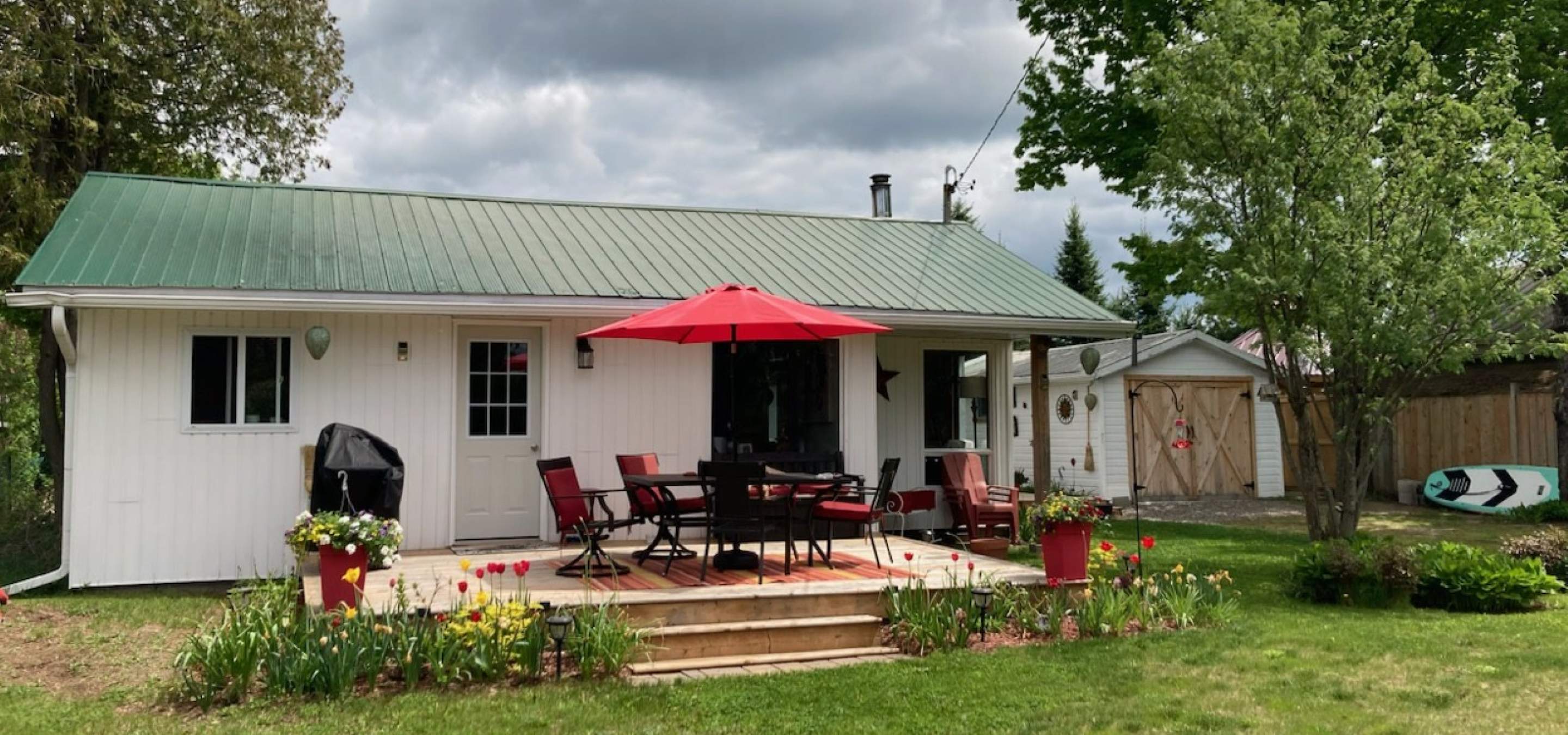 white bungalow with deck that has a patio table and chairs with red umbrella