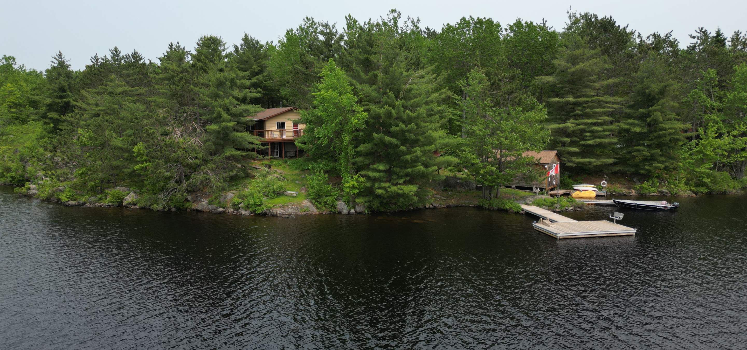 aerial view of cottage in trees with a dock in the water 