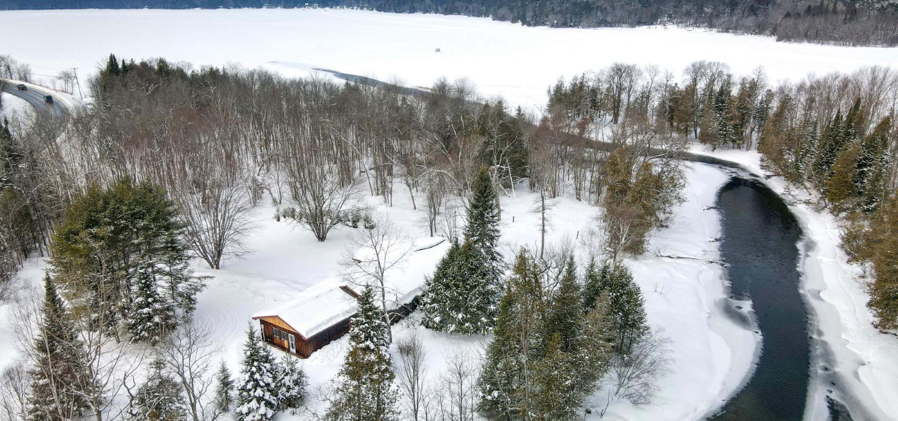 House surrounded by trees with a river leading to the lake. Snow on the ground
