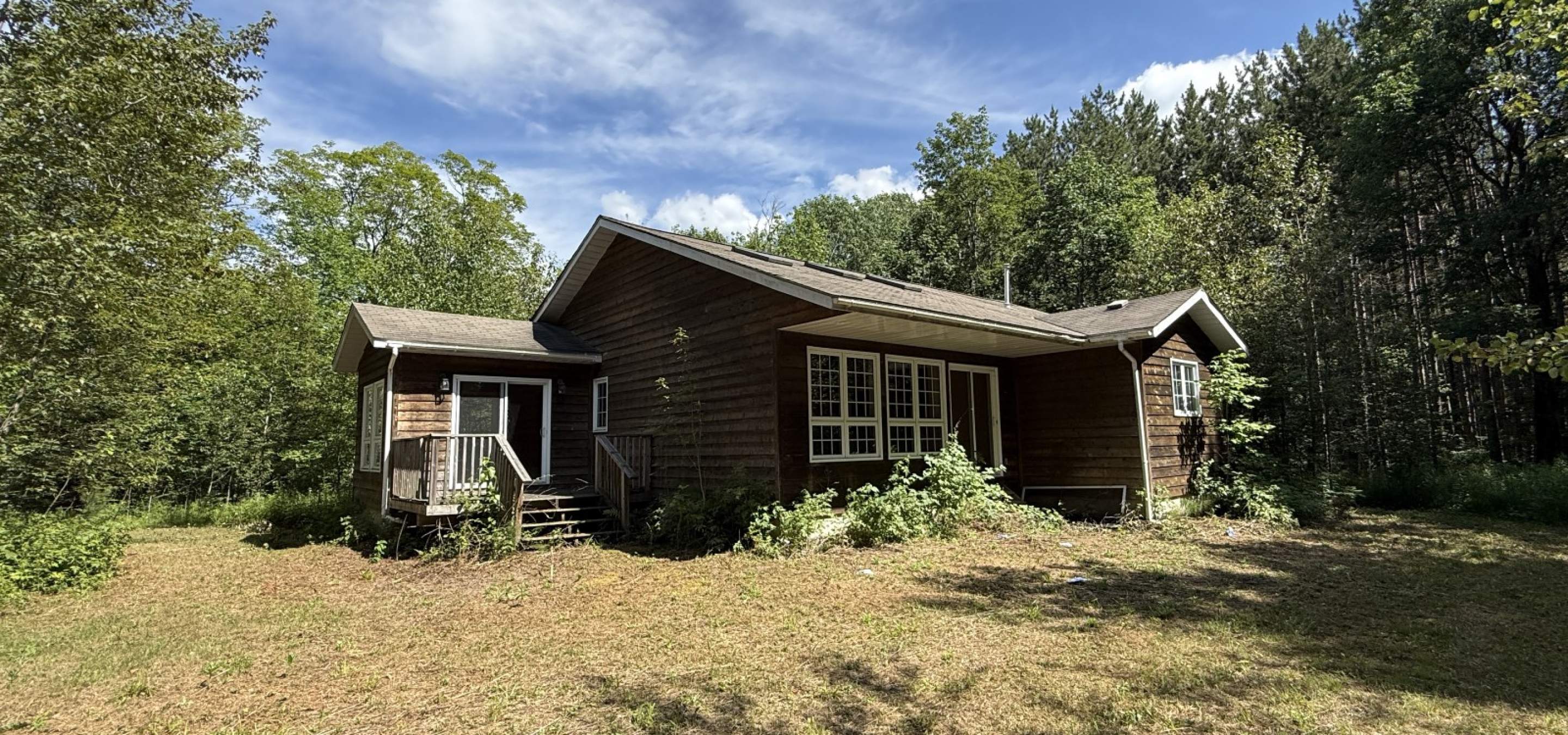 Brown house with small deck, brown grass and trees.