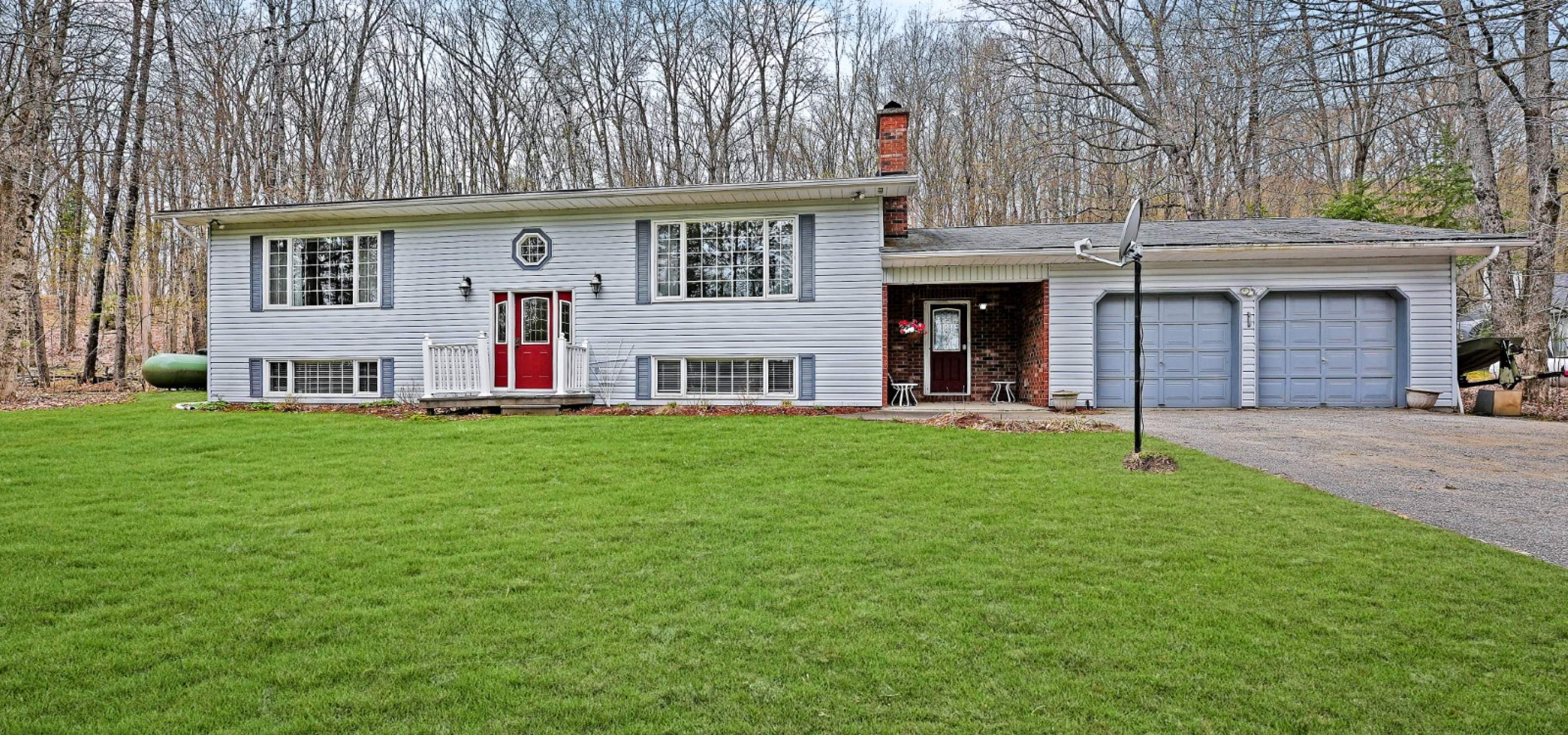 White sided home with a red front door, breeze way and double car garage. Flat green lawn and paved drive way. 