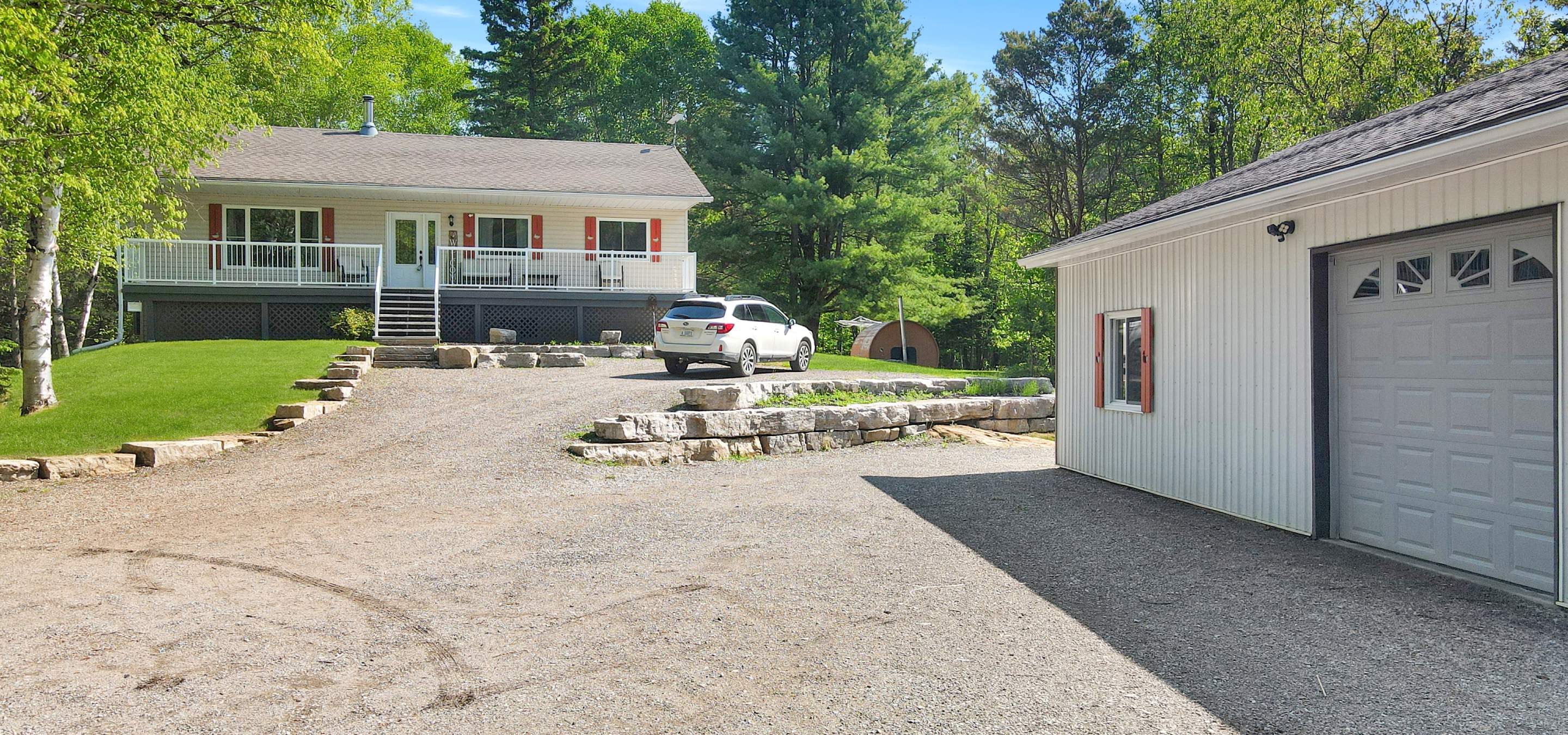 front of a house with a covered front porch, gravel parking area and trees surrounding.