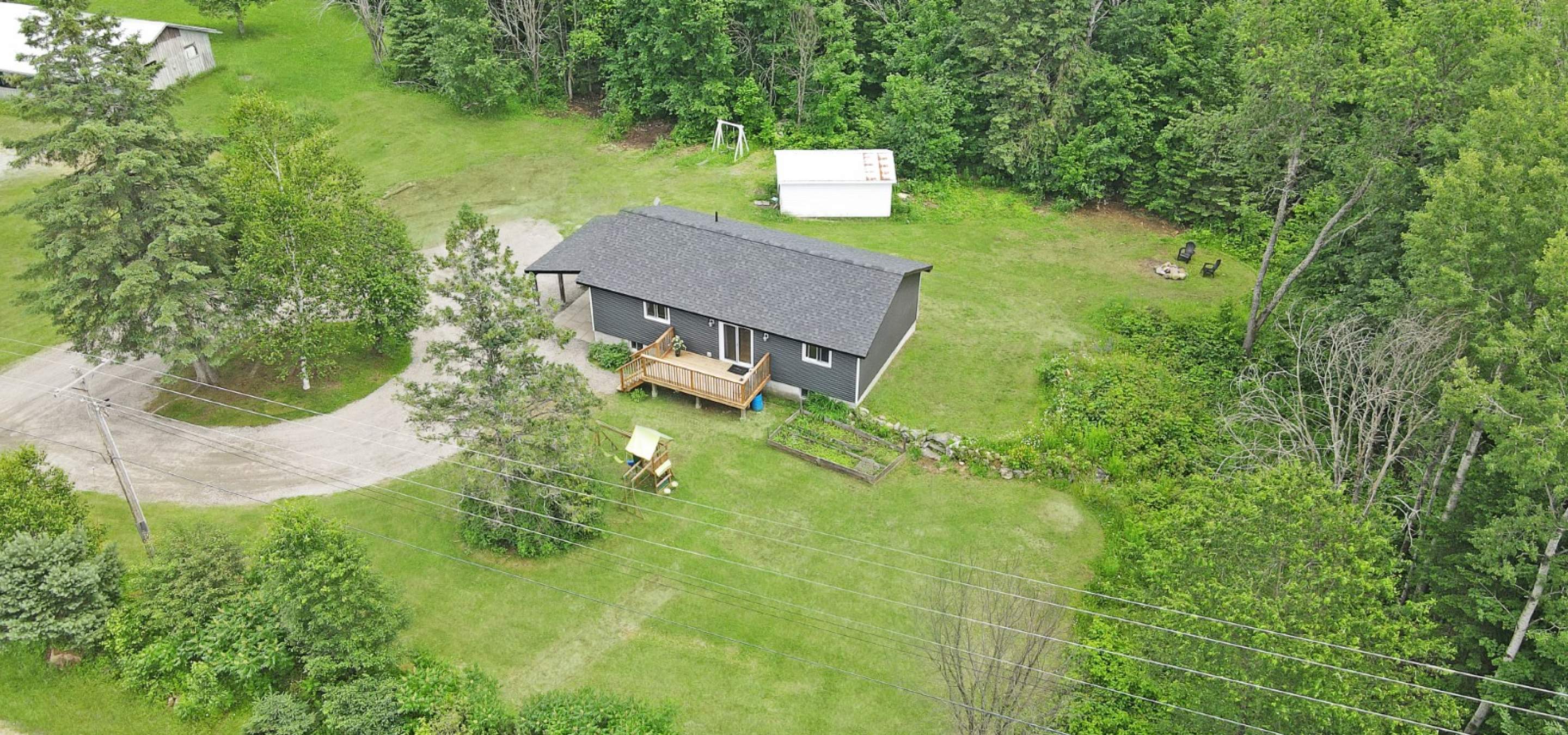 A dark grey bungalow surrounded by grass with trees, and a circular laneway.