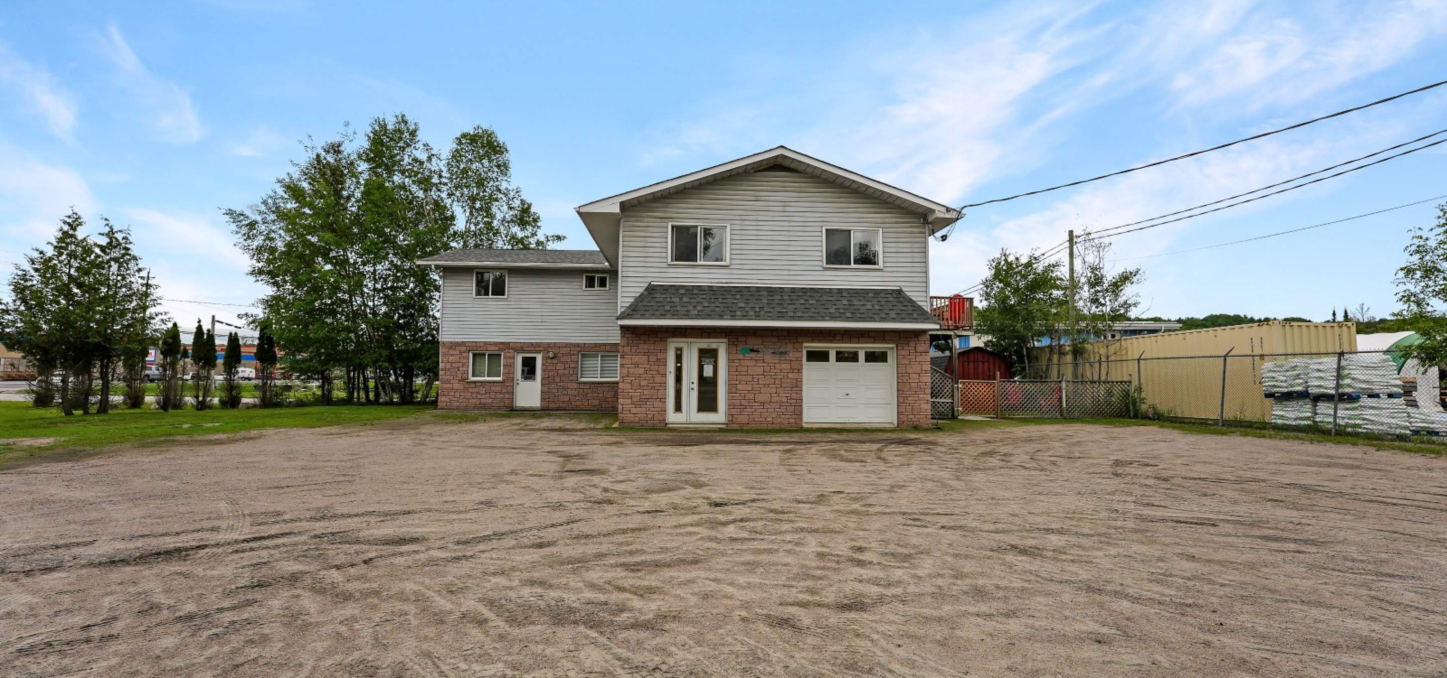 Red brick on bottom level and siding on top level, gravel parking lot and blue sky