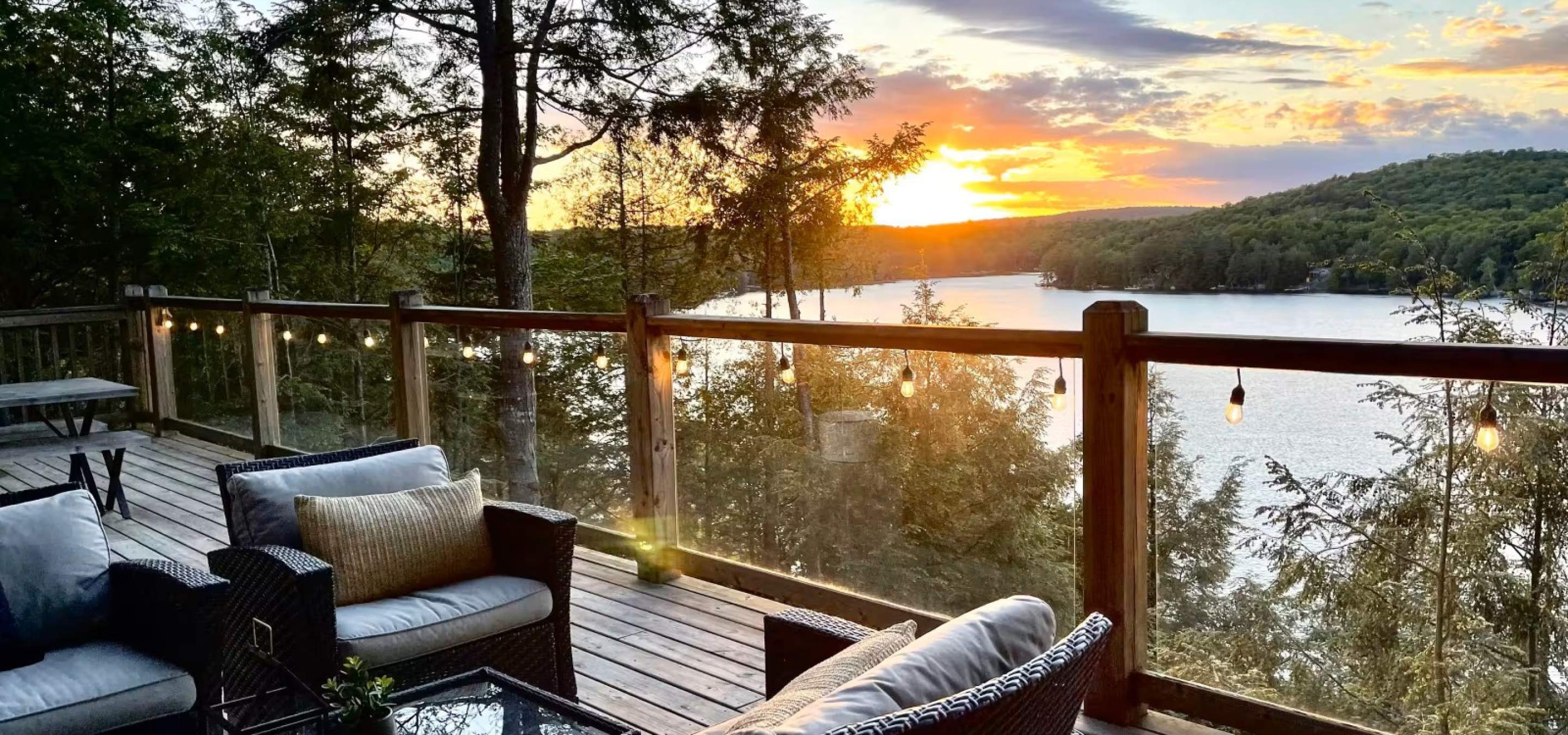 View of the lake with a sunset. Glass railing and 2 chairs, and a couch on the deck.