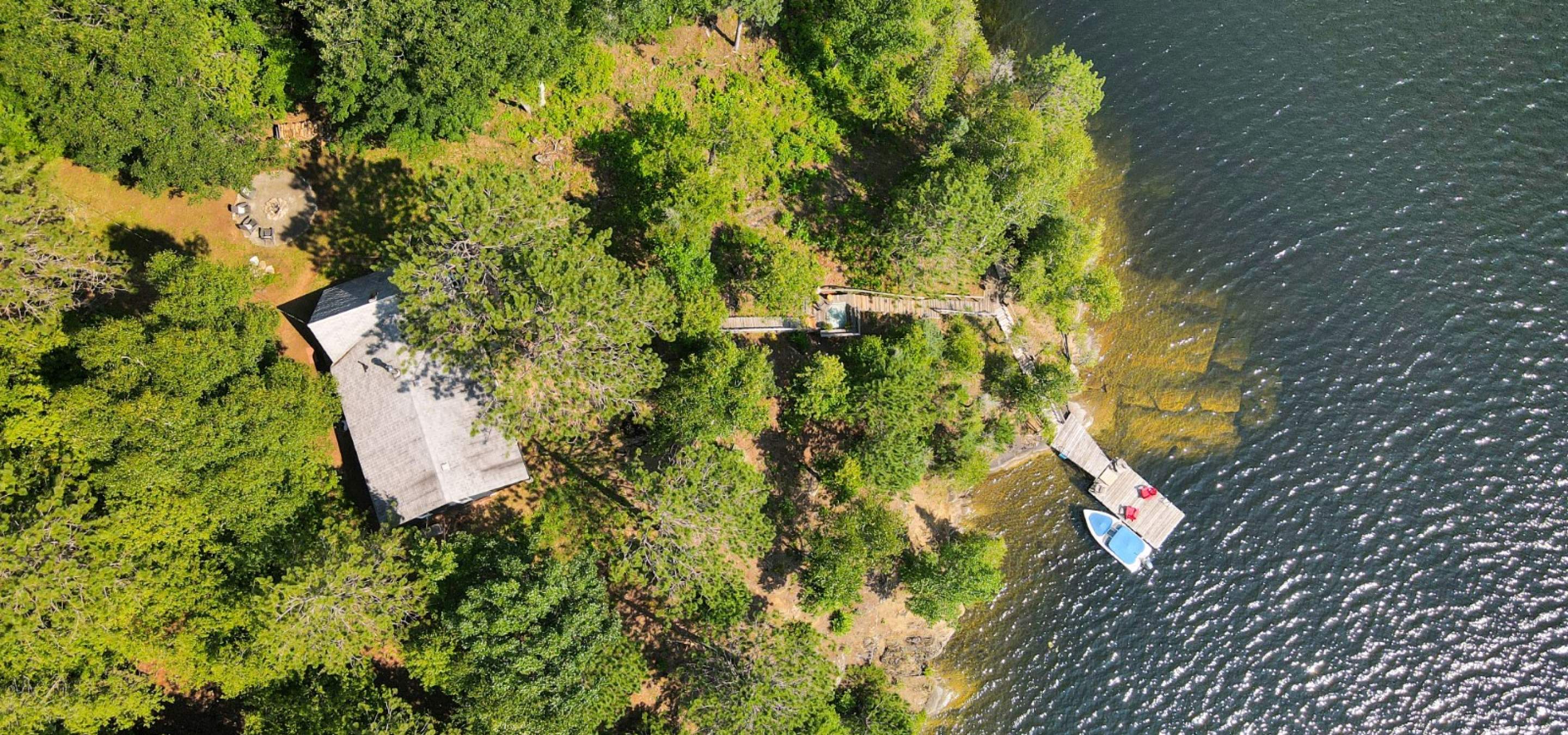 Forested point lot with dock and boat in the water, cottage roof and stairs to the lake