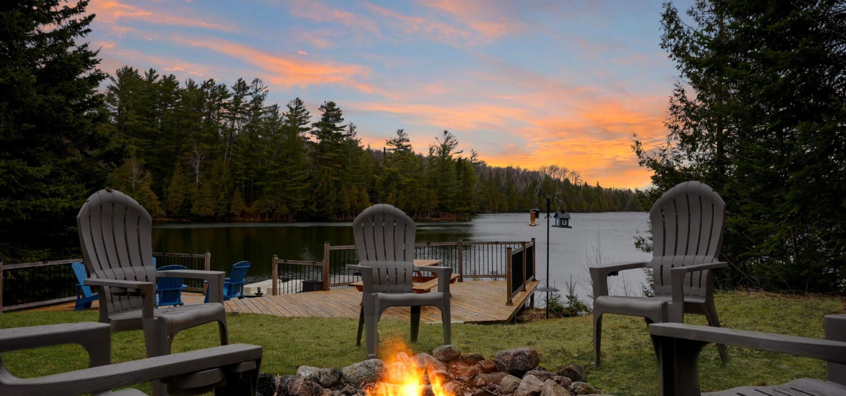 Chairs in front of a fire by the lake. 